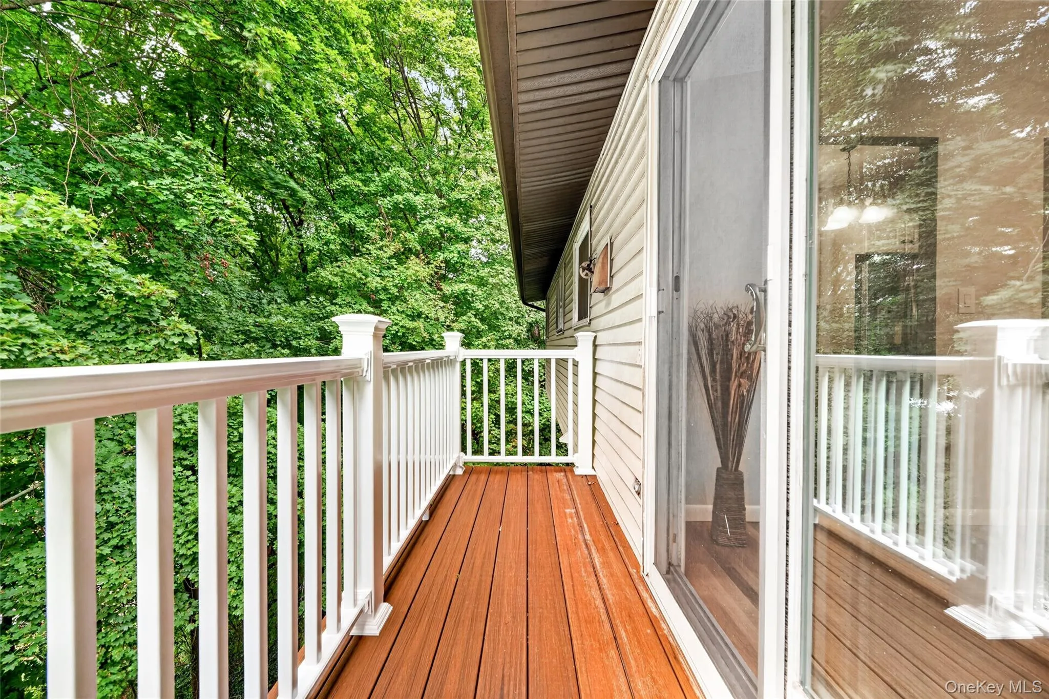 Exterior balcony with wood-finish decking, white railings, and siding Exterior balcony with wood-finish decking, white railings, and siding