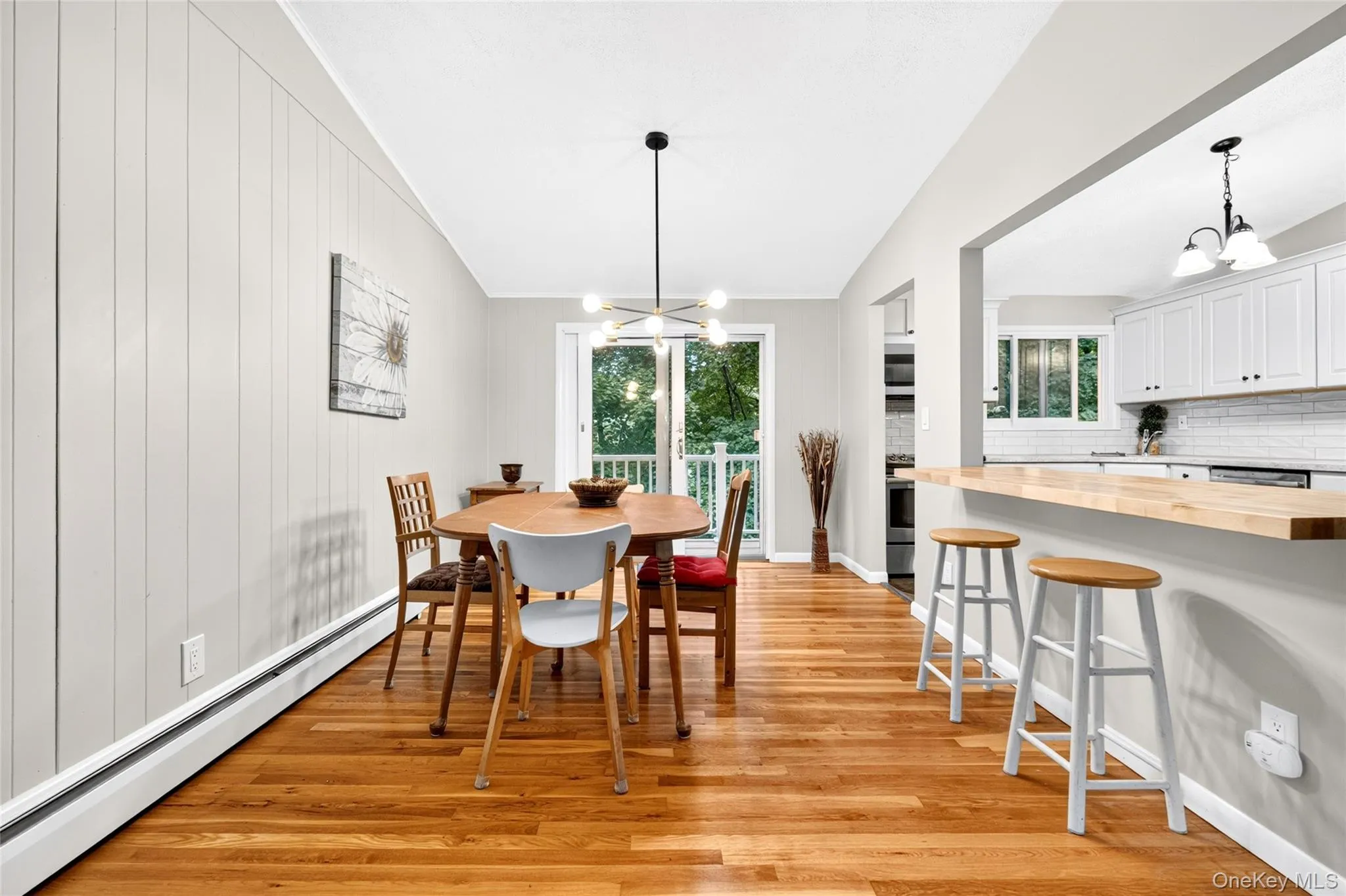 Hardwood flooring, kitchen pass-through with wood-finish countertop, white cabinetry with black hardware, white subway tile backsplash, and sliding glass door Hardwood flooring, kitchen pass-through with wood-finish countertop, white cabinetry with black hardware, white subway tile backsplash, and sliding glass door