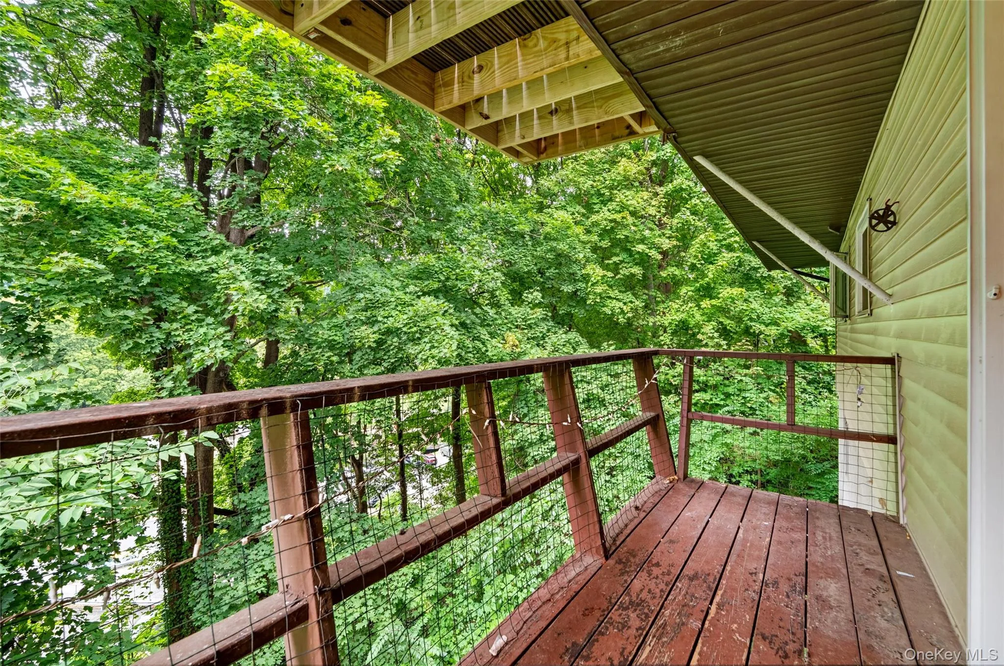 Upper-level wood deck with wire railing, surrounded by mature trees Upper-level wood deck with wire railing, surrounded by mature trees