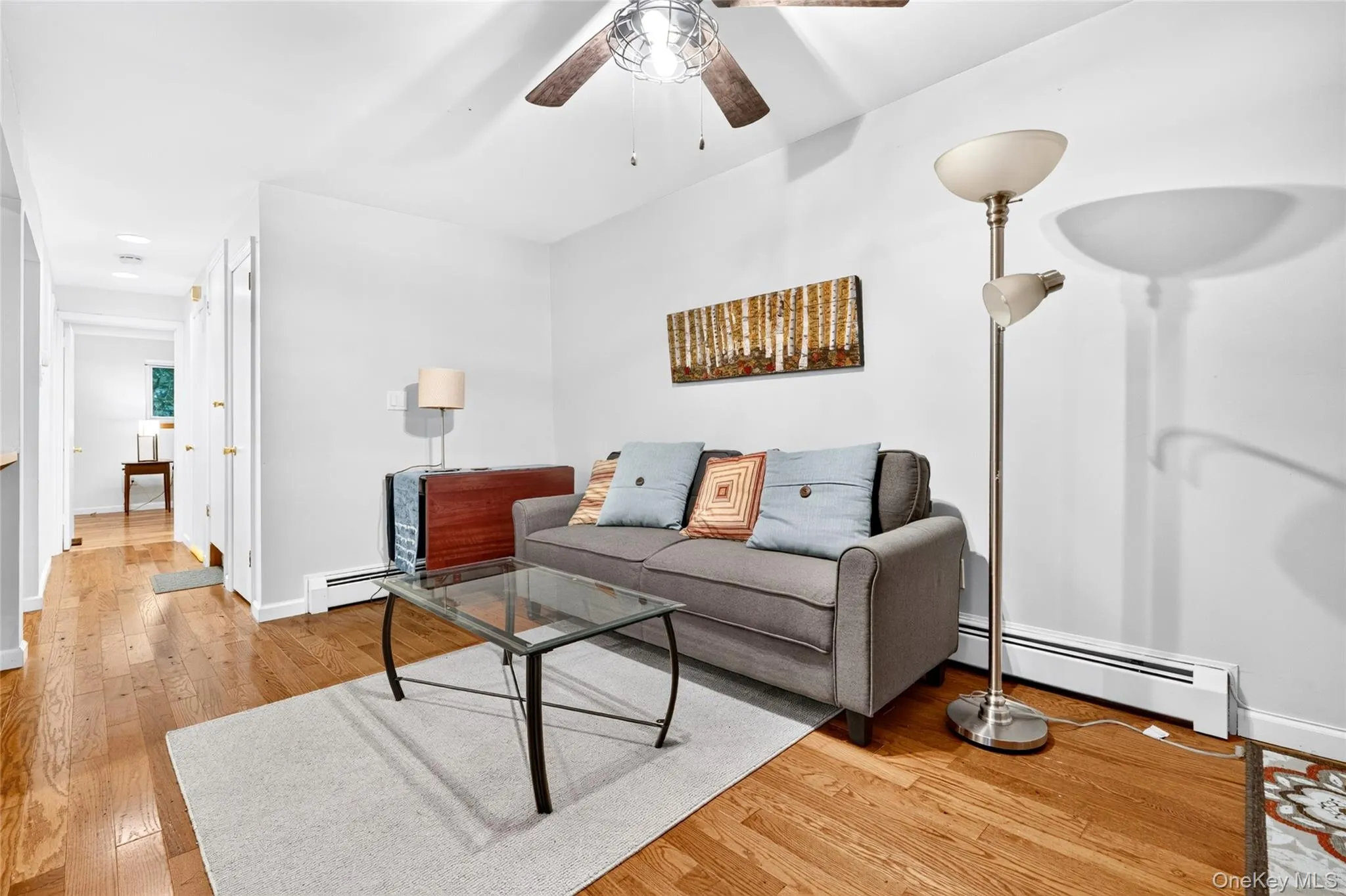 Hardwood flooring, overhead ceiling fan, white baseboard heating, and a white wall finish Hardwood flooring, overhead ceiling fan, white baseboard heating, and a white wall finish