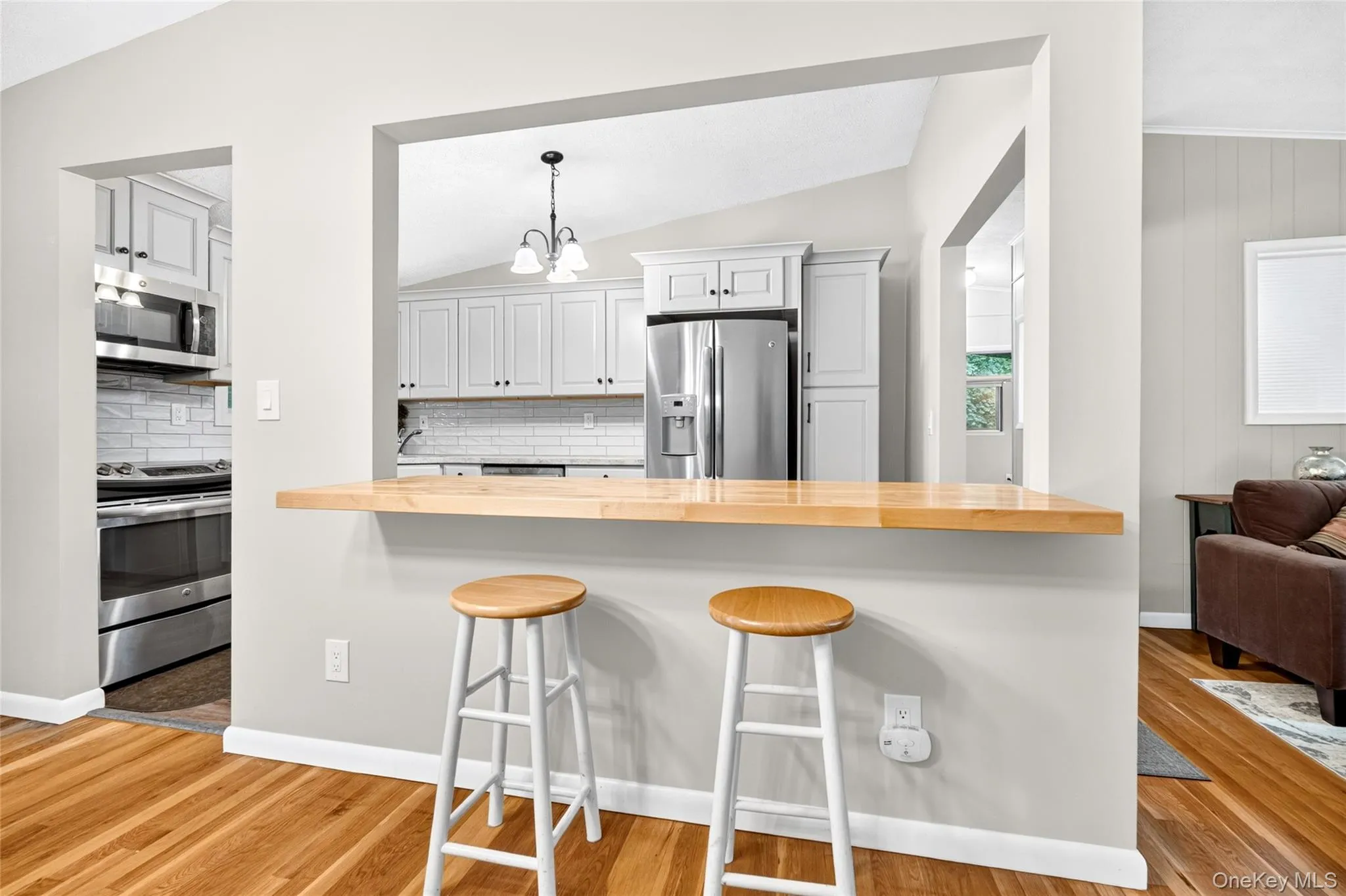 Kitchen pass-through with a natural wood-finish countertop, stainless steel appliances, white subway tile backsplash, and light gray cabinetry Kitchen pass-through with a natural wood-finish countertop, stainless steel appliances, white subway tile backsplash, and light gray cabinetry