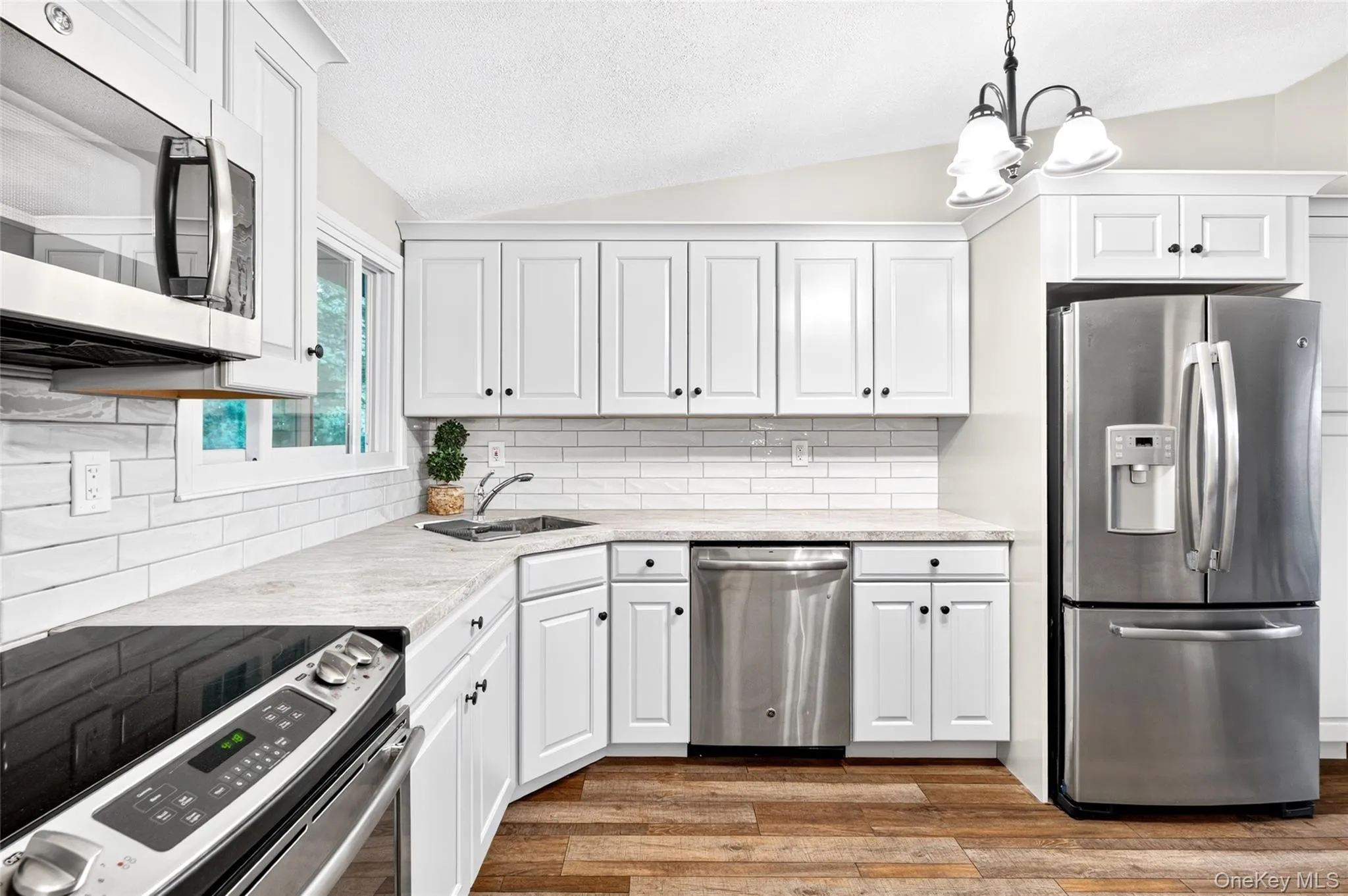 Kitchen featuring white cabinetry, subway tile backsplash, stainless steel appliances, and wood-finish flooring Kitchen featuring white cabinetry, subway tile backsplash, stainless steel appliances, and wood-finish flooring