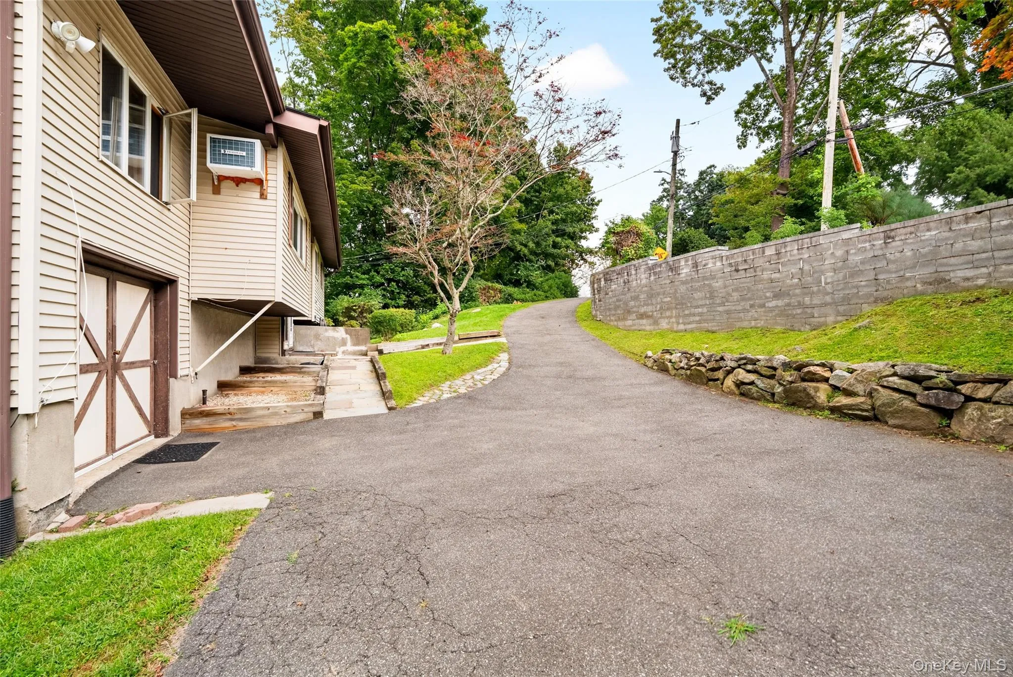 Paved driveway leading to a residence with siding exterior, featuring an entry door with decorative cross bracing and an exposed foundation Paved driveway leading to a residence with siding exterior, featuring an entry door with decorative cross bracing and an exposed foundation