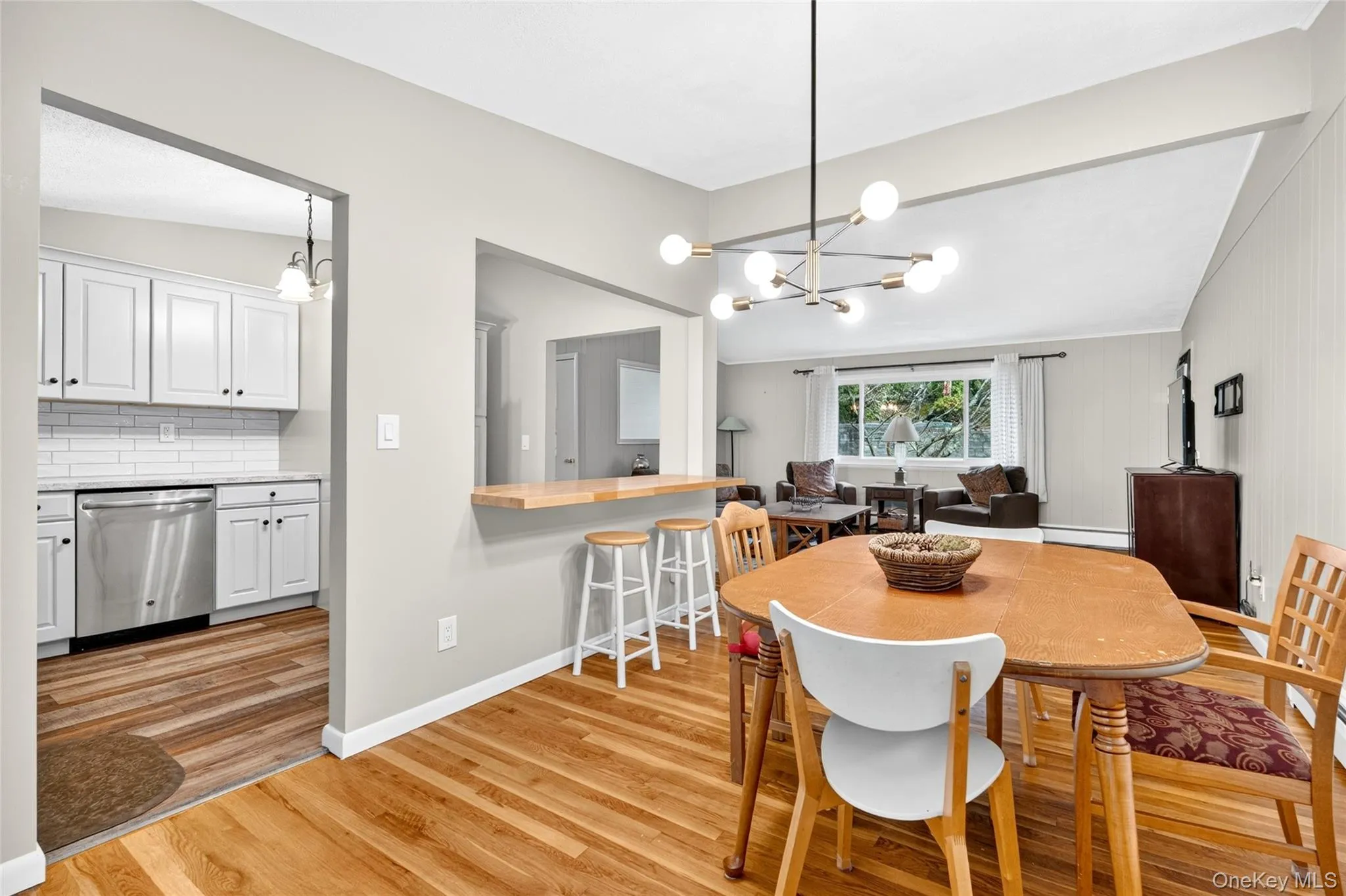 Hardwood flooring, kitchen pass-through with breakfast bar, white shaker cabinetry, stainless steel dishwasher, and white subway tile backsplash Hardwood flooring, kitchen pass-through with breakfast bar, white shaker cabinetry, stainless steel dishwasher, and white subway tile backsplash