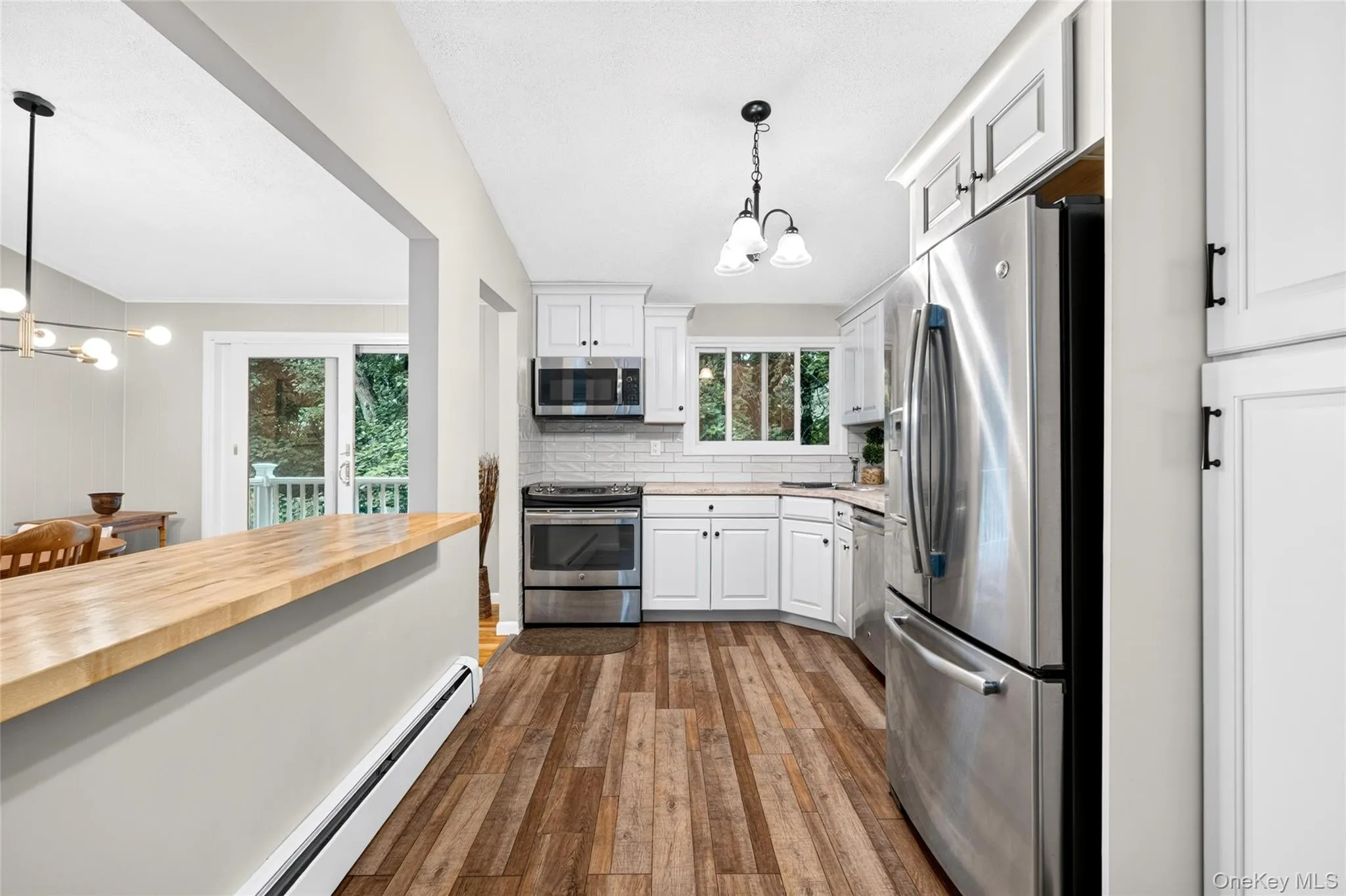 White shaker cabinetry, stainless steel appliances, wood-finish flooring, butcher block counter, and a tile backsplash White shaker cabinetry, stainless steel appliances, wood-finish flooring, butcher block counter, and a tile backsplash