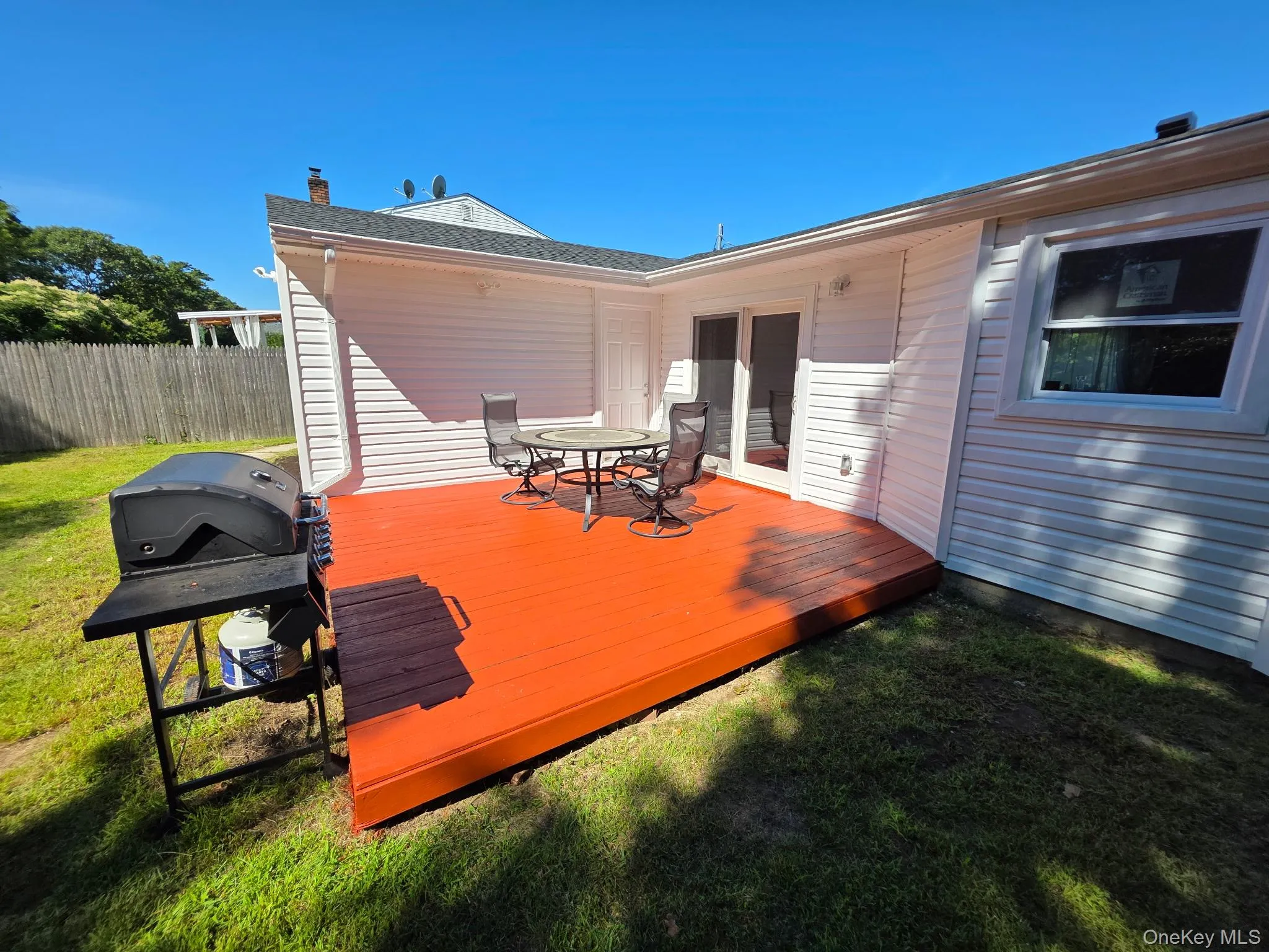 Spacious outdoor deck with a vibrant red-orange finish, adjacent to a sliding glass door and a window with white trim Spacious outdoor deck with a vibrant red-orange finish, adjacent to a sliding glass door and a window with white trim