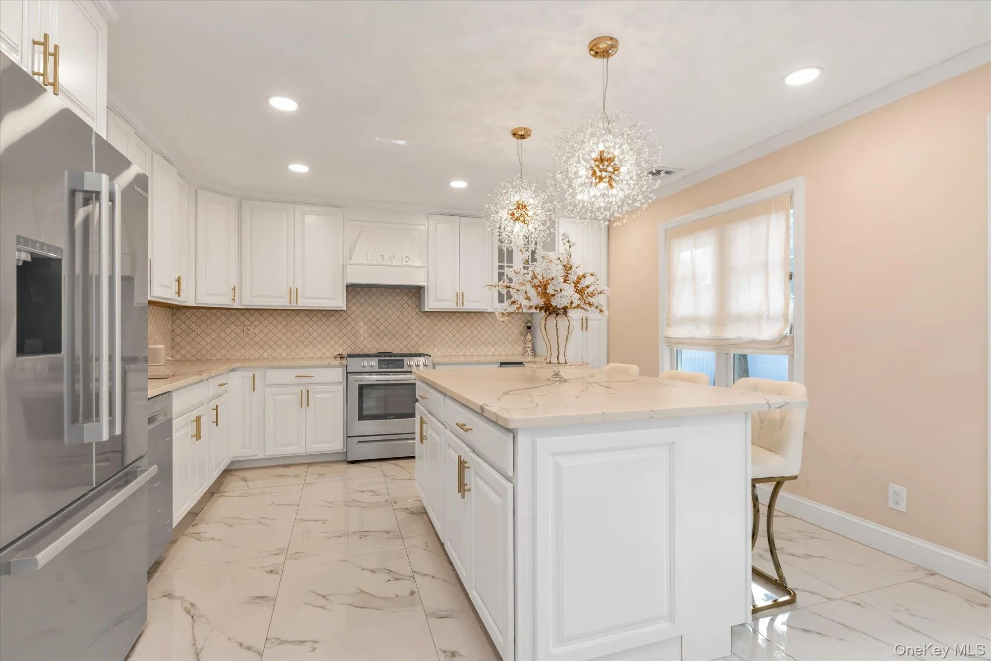 White cabinetry with gold-tone hardware and faucet taps, gas stove, stainless steel appliances, white quartz countertops, central island with storage, and beautiful white porcelain floor tile White cabinetry with gold-tone hardware and faucet taps, gas stove, stainless steel appliances, white quartz countertops, central island with storage, and beautiful white porcelain floor tile