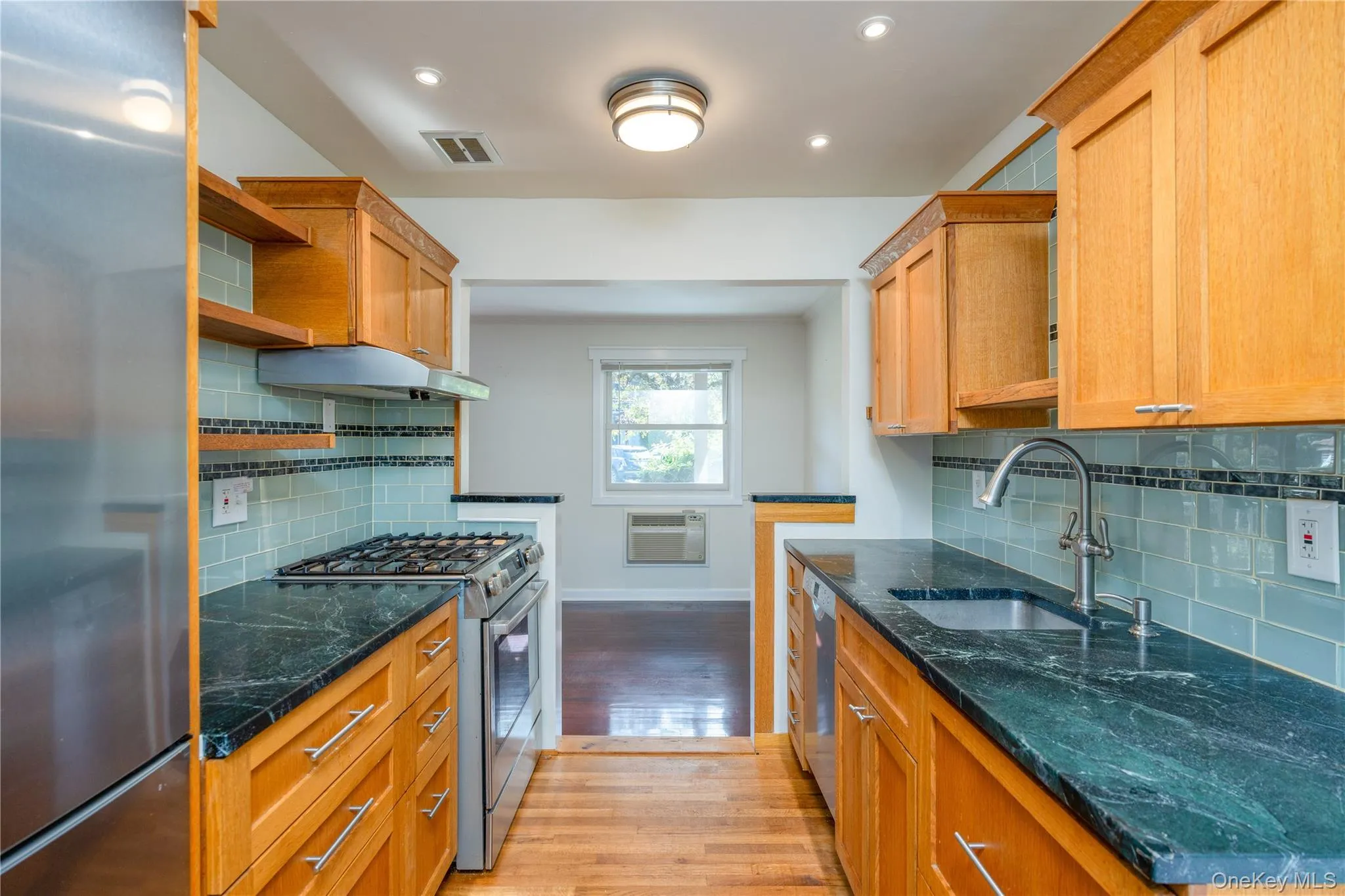 Galley kitchen featuring wood cabinetry, dark stone countertops, a subway tile backsplash, and stainless steel appliances Galley kitchen featuring wood cabinetry, dark stone countertops, a subway tile backsplash, and stainless steel appliances