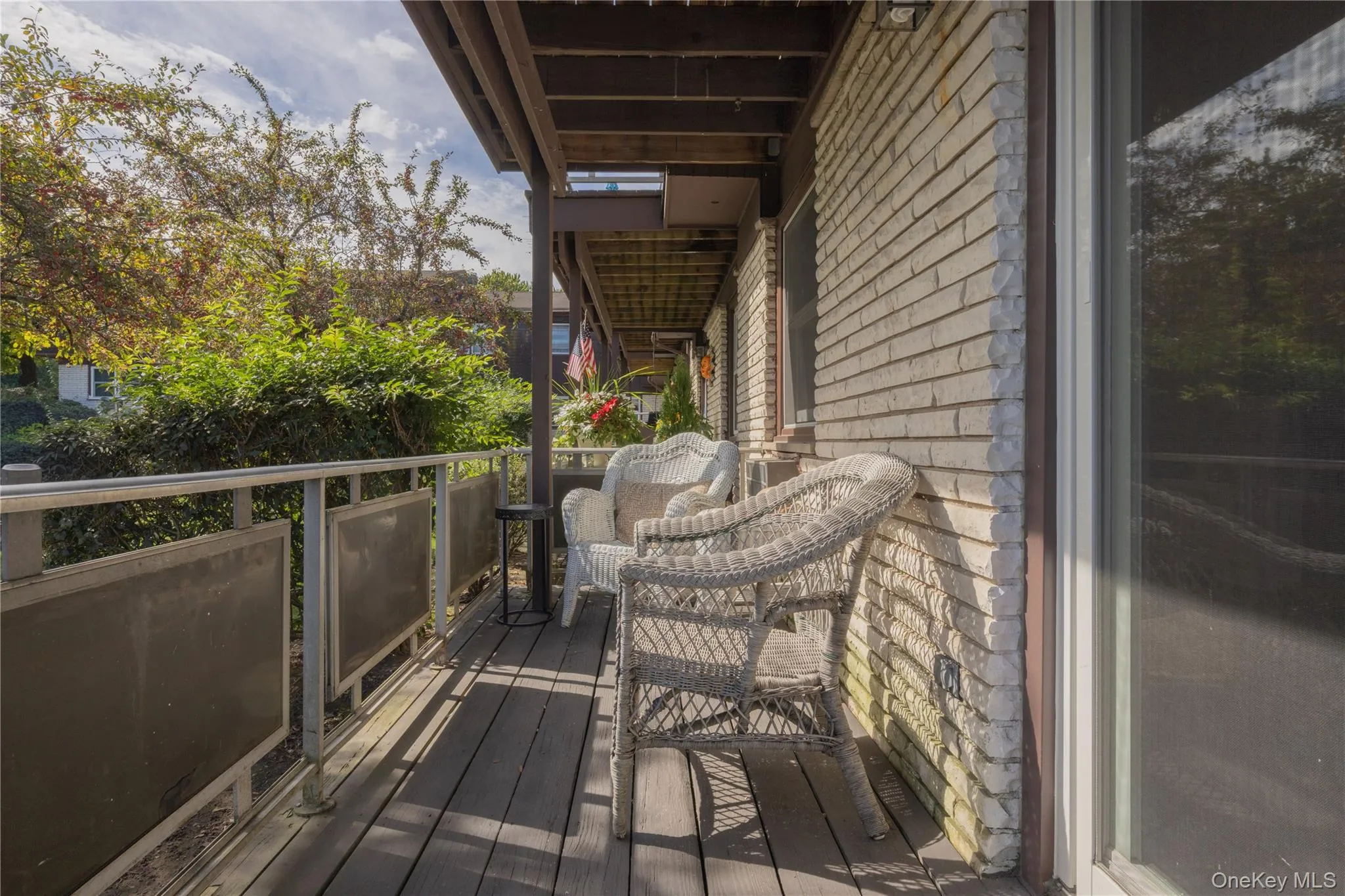 Covered outdoor deck with wood-finish flooring, featuring a solid brick exterior wall and a glass sliding door Covered outdoor deck with wood-finish flooring, featuring a solid brick exterior wall and a glass sliding door