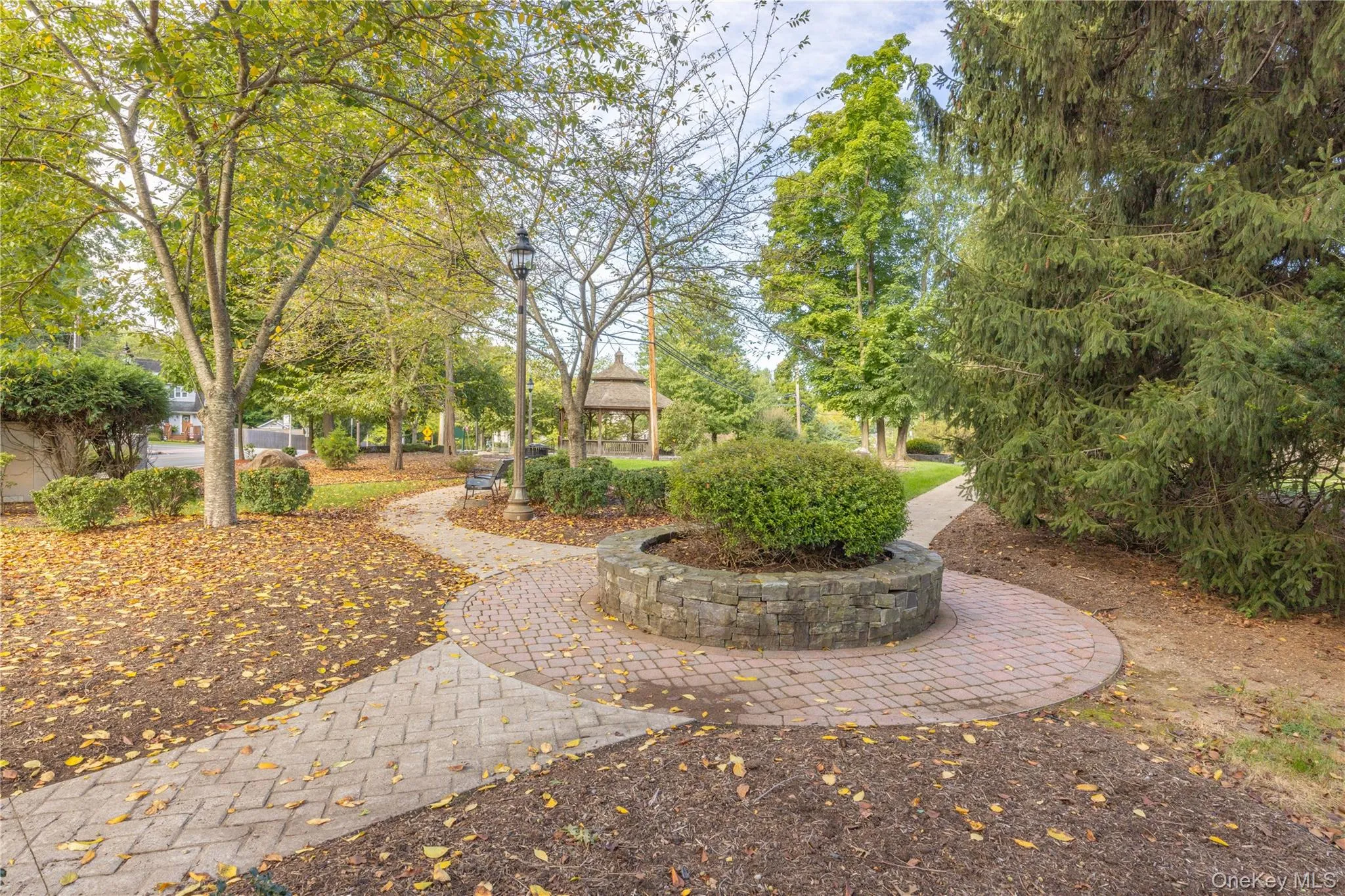 Paved brick pathways, mature trees, manicured shrubs, a stone-faced planter, and a distant gazebo Paved brick pathways, mature trees, manicured shrubs, a stone-faced planter, and a distant gazebo