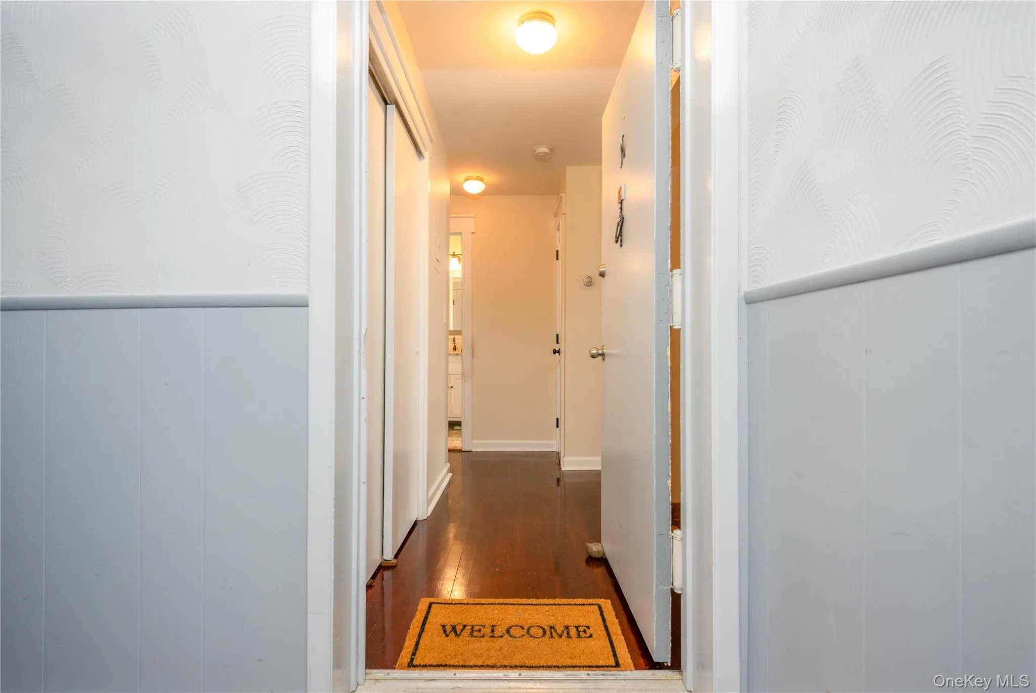 Hallway with wood-finish flooring, two-tone wall treatment, and overhead lighting Hallway with wood-finish flooring, two-tone wall treatment, and overhead lighting