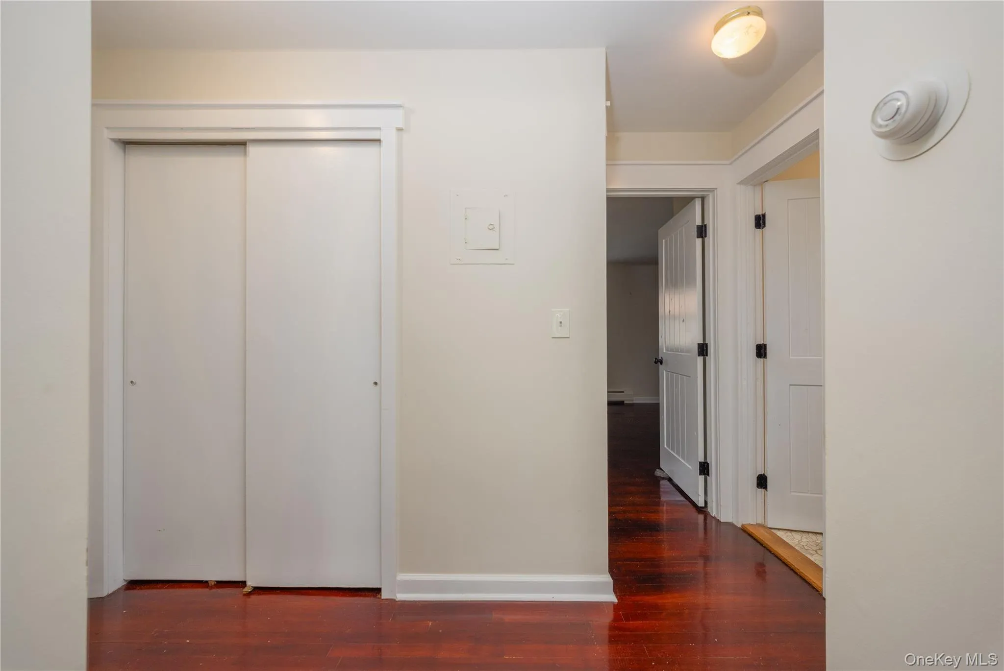 Hardwood-finish flooring, white sliding closet doors, white paneled interior doors, and a flush mount ceiling light fixture Hardwood-finish flooring, white sliding closet doors, white paneled interior doors, and a flush mount ceiling light fixture
