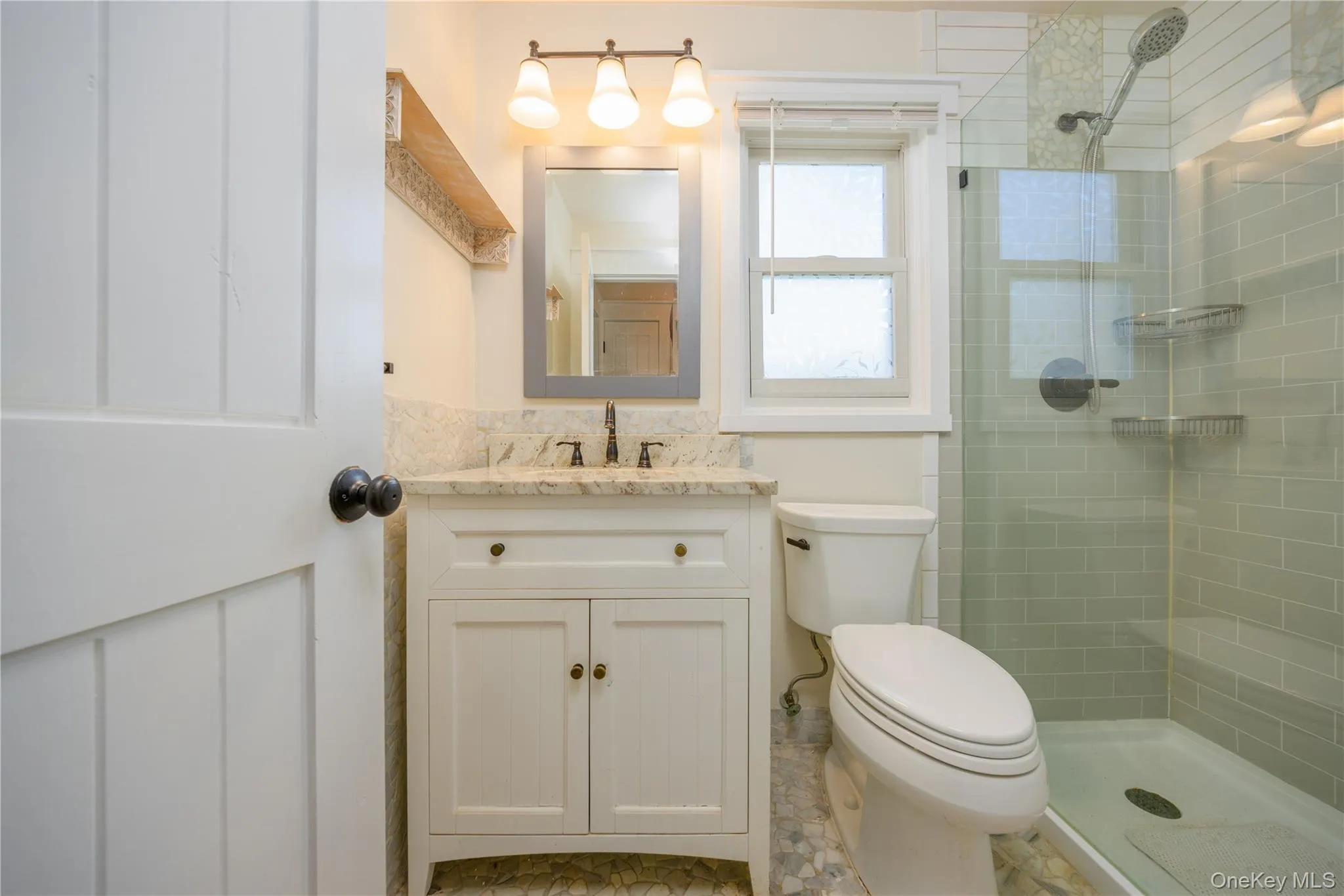 White shaker-style vanity with a stone countertop, framed mirror, and a three-light fixture White shaker-style vanity with a stone countertop, framed mirror, and a three-light fixture