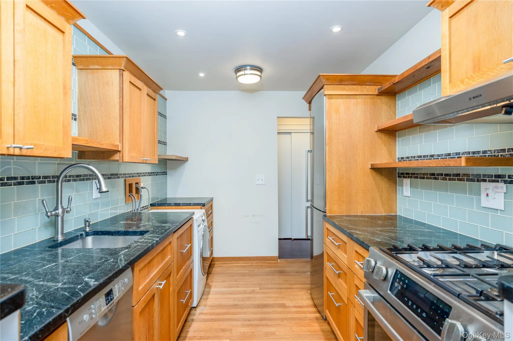 Kitchen featuring wood cabinetry, stainless steel appliances, dark stone countertops, and a subway tile backsplash Kitchen featuring wood cabinetry, stainless steel appliances, dark stone countertops, and a subway tile backsplash