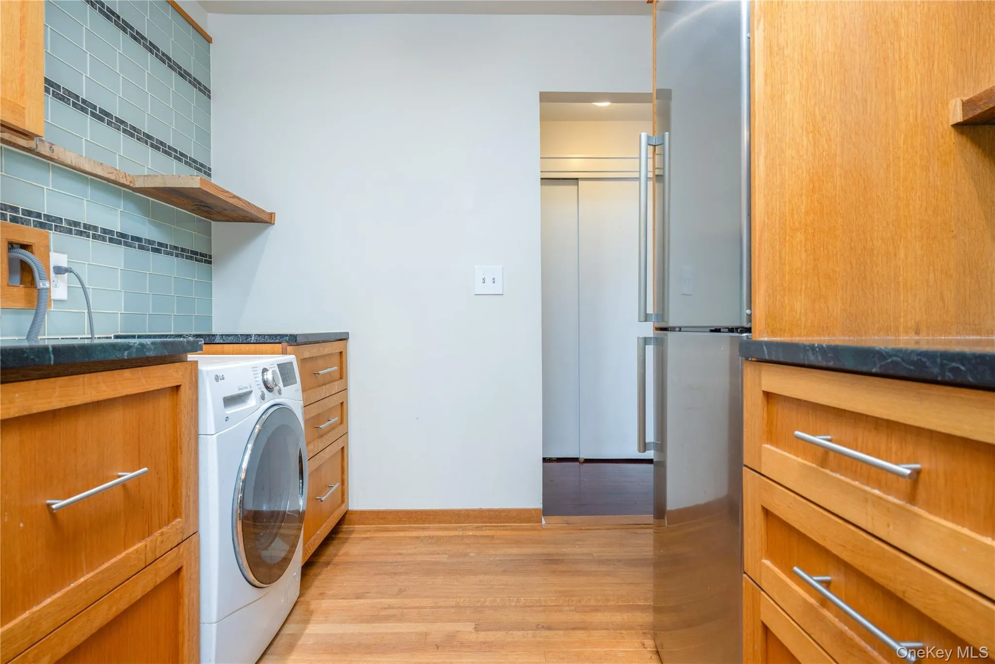 Wood-finish flooring, custom wood cabinetry, dark countertops, and a tiled backsplash with accent banding Wood-finish flooring, custom wood cabinetry, dark countertops, and a tiled backsplash with accent banding
