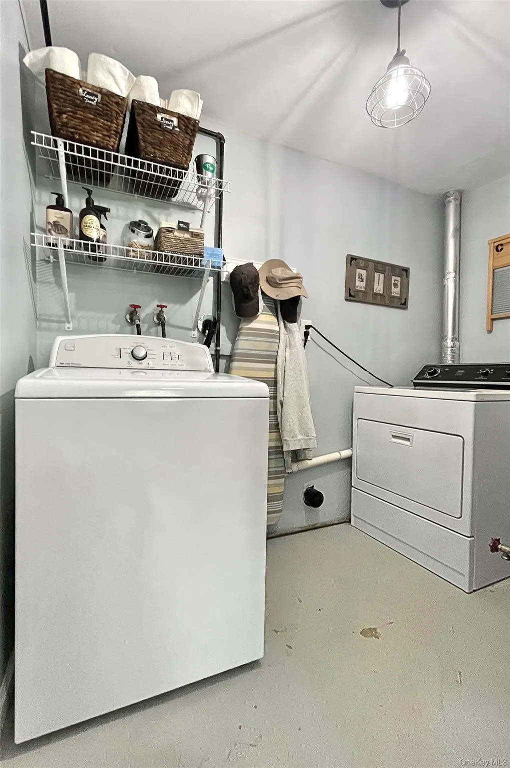 Laundry area with painted concrete flooring, two wall-mounted wire shelving units, and a ceiling-mounted caged light fixture Laundry area with painted concrete flooring, two wall-mounted wire shelving units, and a ceiling-mounted caged light fixture