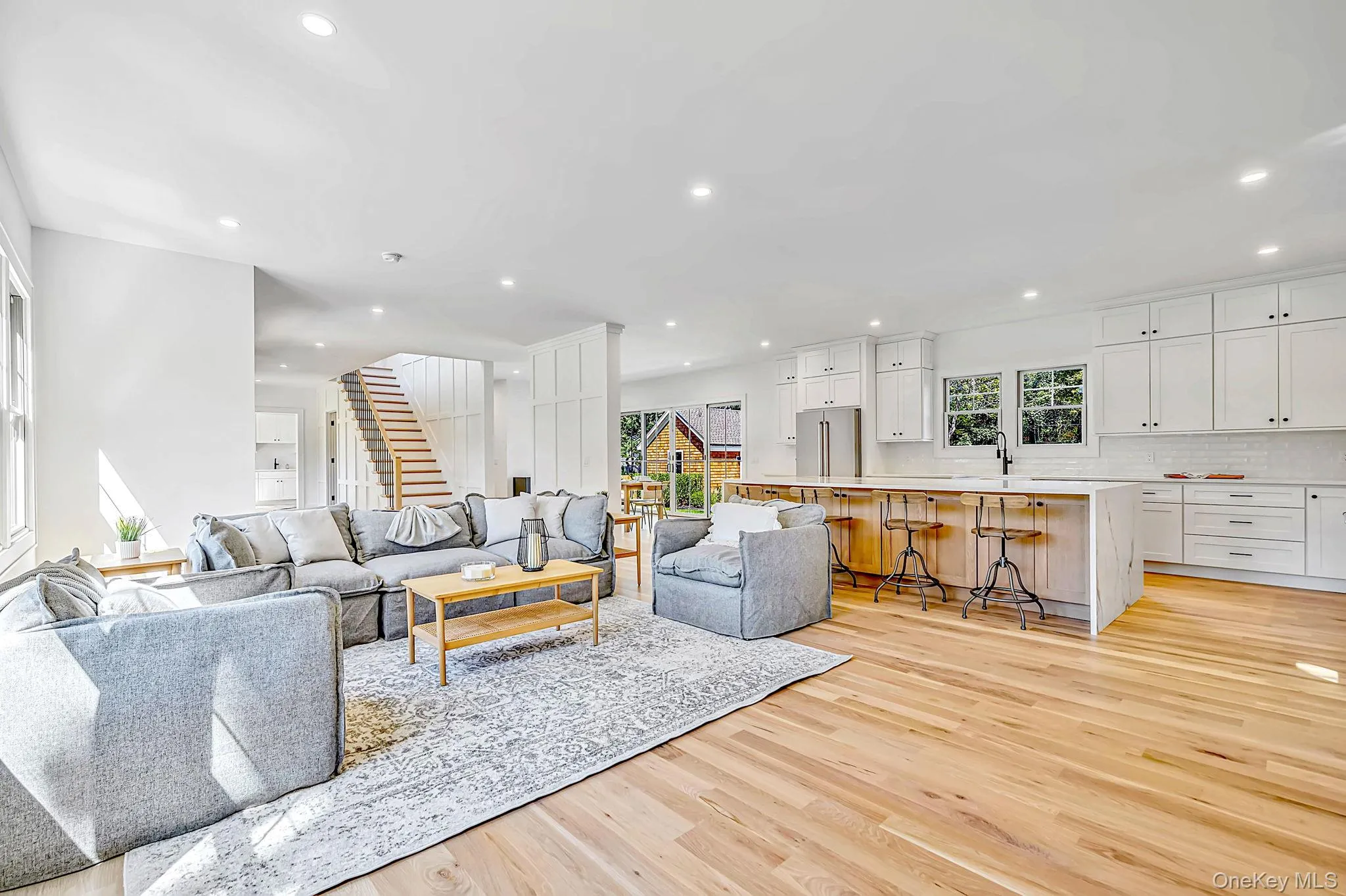 Open-concept living space featuring wood-finish flooring, recessed lighting, and a kitchen with white cabinetry and a large island Open-concept living space featuring wood-finish flooring, recessed lighting, and a kitchen with white cabinetry and a large island