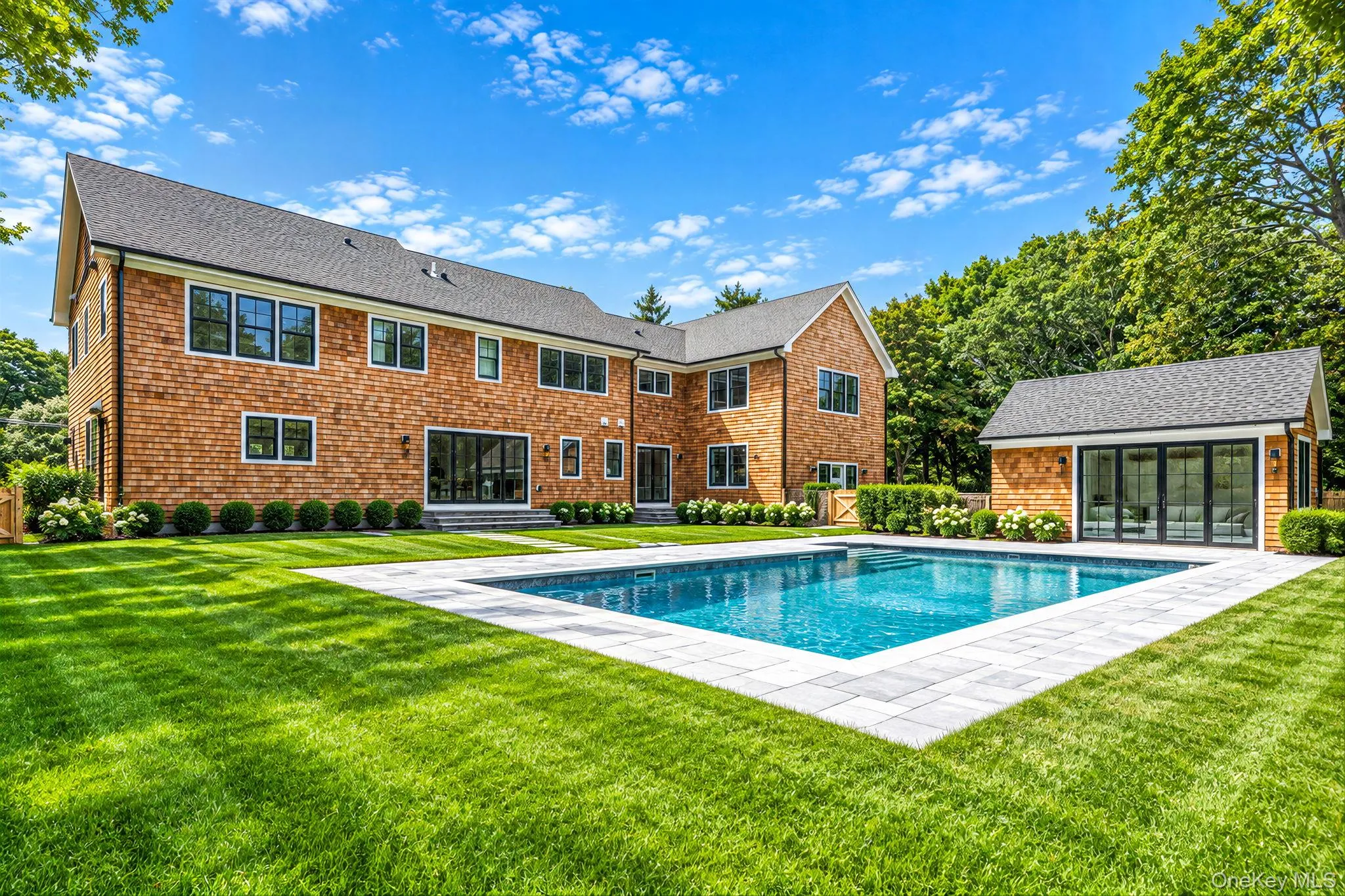 Expansive backyard featuring a rectangular swimming pool, paver surround, manicured lawn, and a pool house with bi-fold glass doors Expansive backyard featuring a rectangular swimming pool, paver surround, manicured lawn, and a pool house with bi-fold glass doors