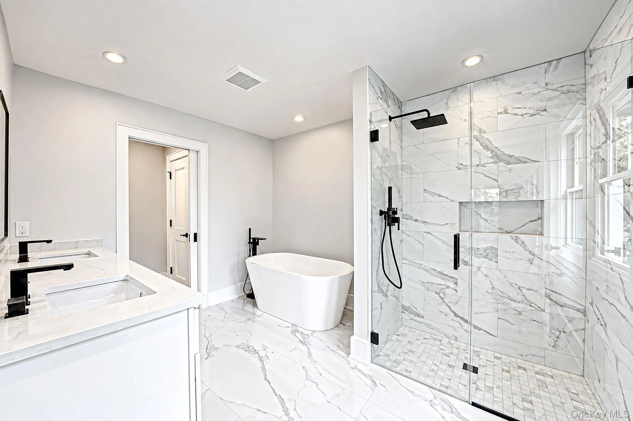 Freestanding soaking tub, walk-in shower with glass enclosure, dual vanity with undermount sinks, and marble-look tile flooring Freestanding soaking tub, walk-in shower with glass enclosure, dual vanity with undermount sinks, and marble-look tile flooring