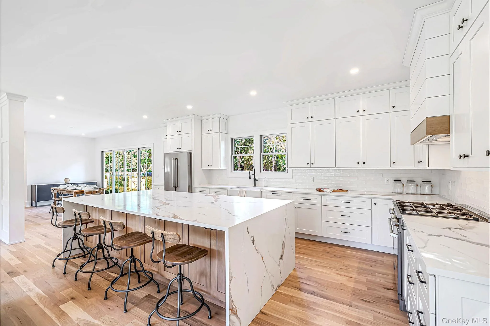 Gourmet kitchen featuring a waterfall island, white shaker cabinetry, stainless steel appliances, a gas range, and wood-finish flooring Gourmet kitchen featuring a waterfall island, white shaker cabinetry, stainless steel appliances, a gas range, and wood-finish flooring