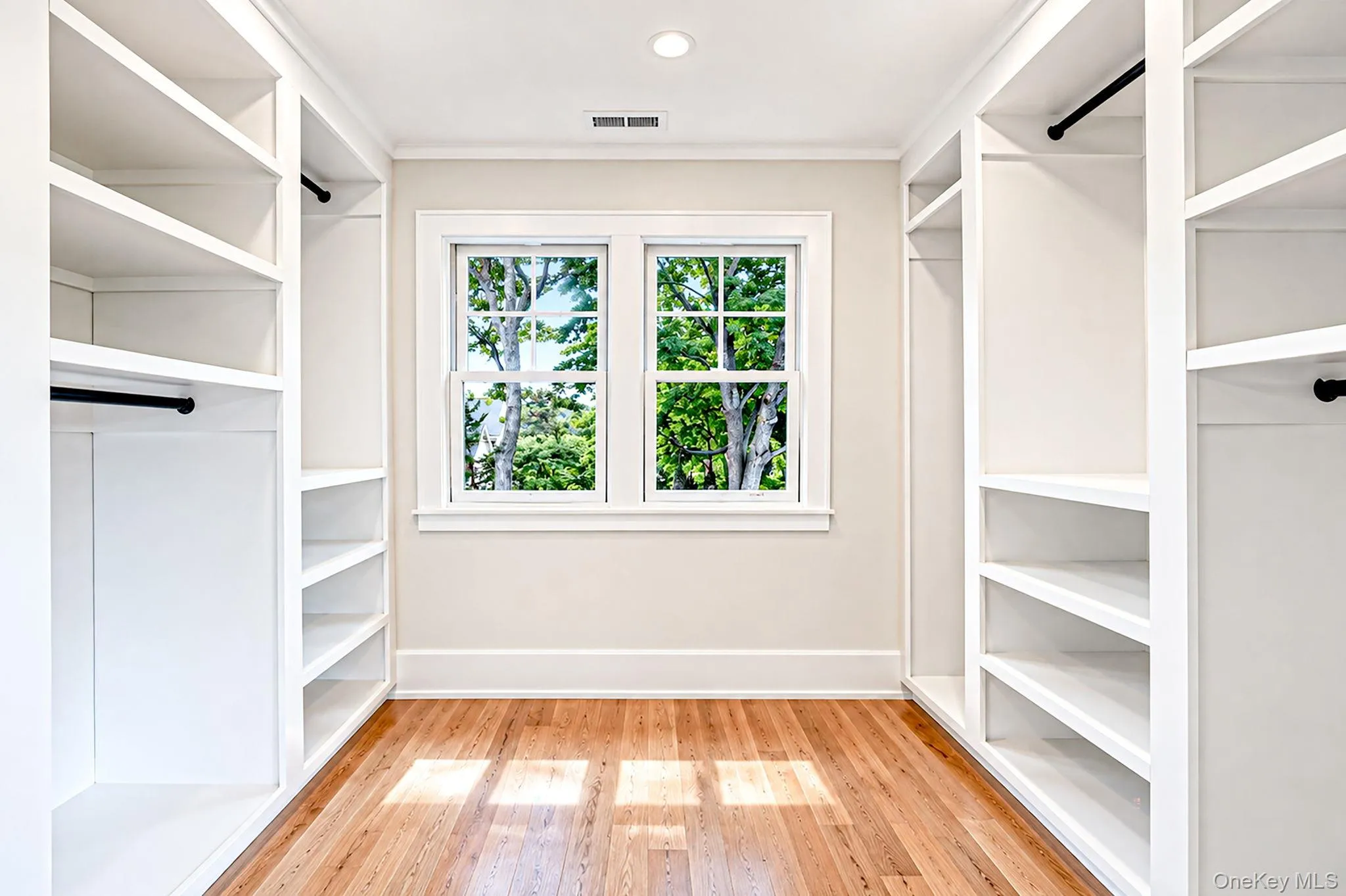 Built-in white shelving and hanging rods, light wood-finish flooring, and a double window Built-in white shelving and hanging rods, light wood-finish flooring, and a double window