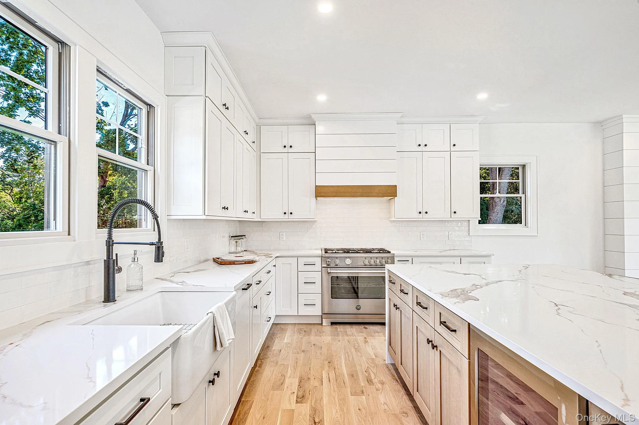 White shaker cabinetry, light wood-finish flooring, white stone countertops, stainless steel range, and a farmhouse sink with a matte black faucet White shaker cabinetry, light wood-finish flooring, white stone countertops, stainless steel range, and a farmhouse sink with a matte black faucet