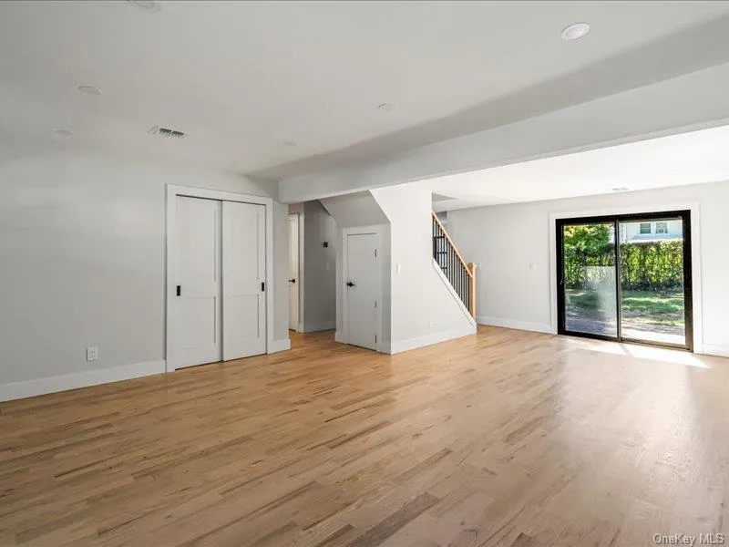 Expansive room featuring wood-finish flooring, recessed lighting, white walls, and a sliding glass door Expansive room featuring wood-finish flooring, recessed lighting, white walls, and a sliding glass door