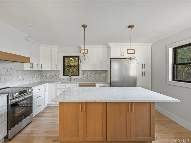 White shaker cabinetry, light wood-finish flooring, full height backsplash, stainless steel appliances, and a central island with a light-colored countertop White shaker cabinetry, light wood-finish flooring, full height backsplash, stainless steel appliances, and a central island with a light-colored countertop