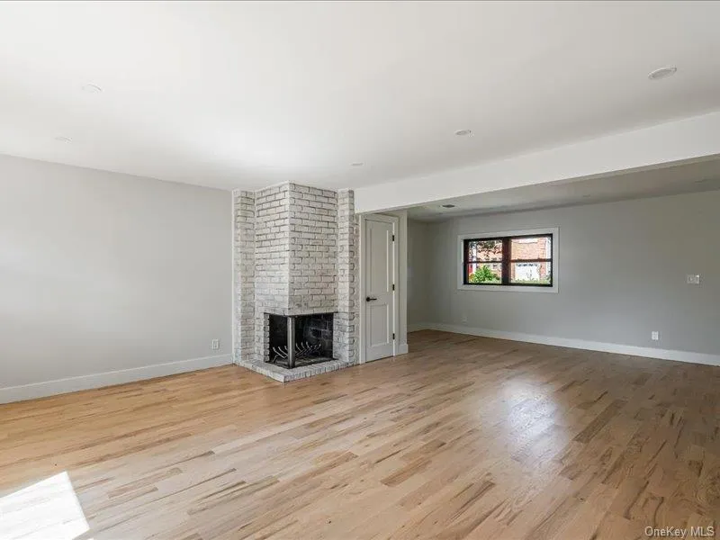 Expansive interior featuring wood-finish flooring, a white-washed brick fireplace, recessed lighting, and a white interior door Expansive interior featuring wood-finish flooring, a white-washed brick fireplace, recessed lighting, and a white interior door