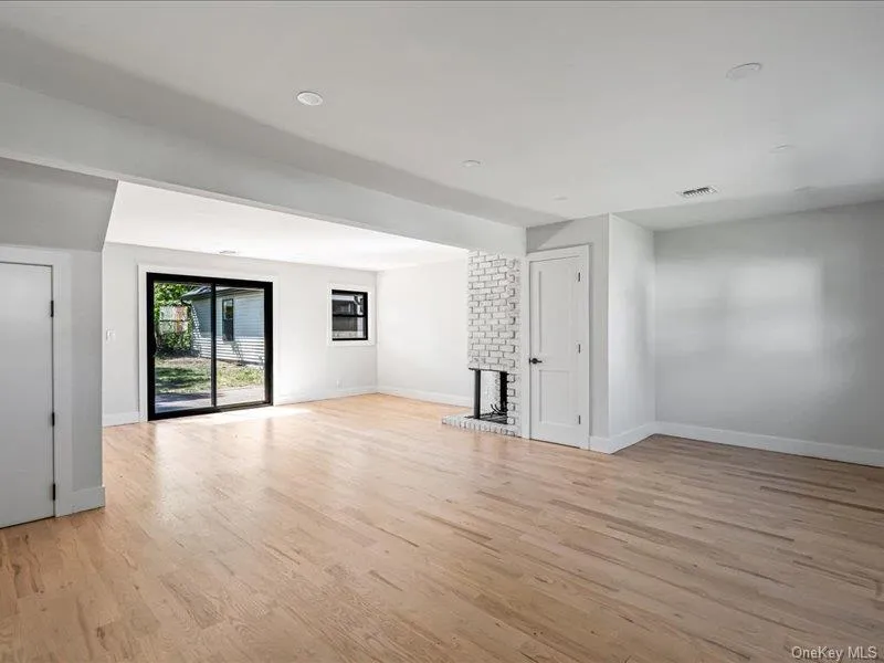 Spacious room featuring light wood-finish flooring, a white-painted brick fireplace, and recessed lighting Spacious room featuring light wood-finish flooring, a white-painted brick fireplace, and recessed lighting