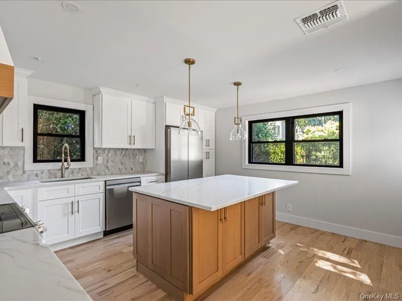Kitchen featuring white cabinetry, a central island with wood-finish cabinetry, light-toned countertops, stainless steel appliances, and wood-finish flooring Kitchen featuring white cabinetry, a central island with wood-finish cabinetry, light-toned countertops, stainless steel appliances, and wood-finish flooring