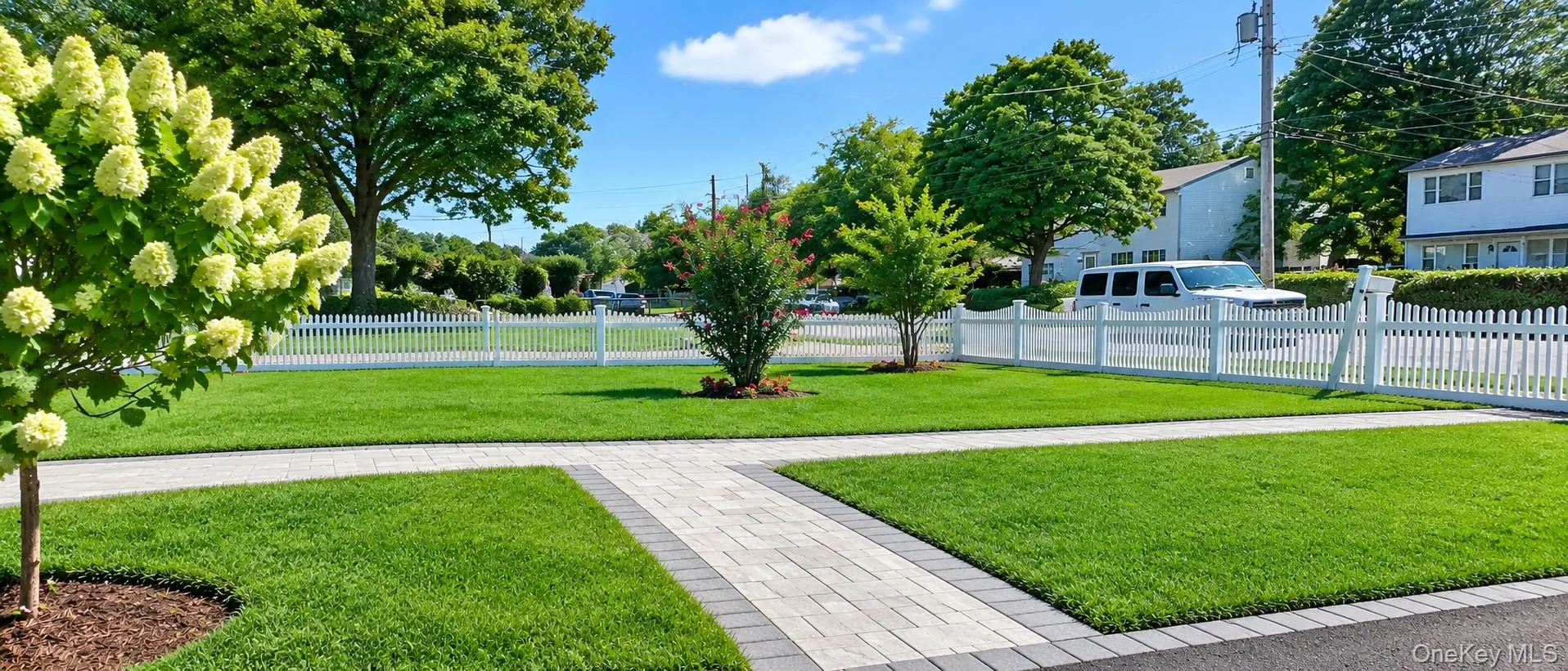Manicured lawn with a paver walkway, trees, and a white picket fence Manicured lawn with a paver walkway, trees, and a white picket fence