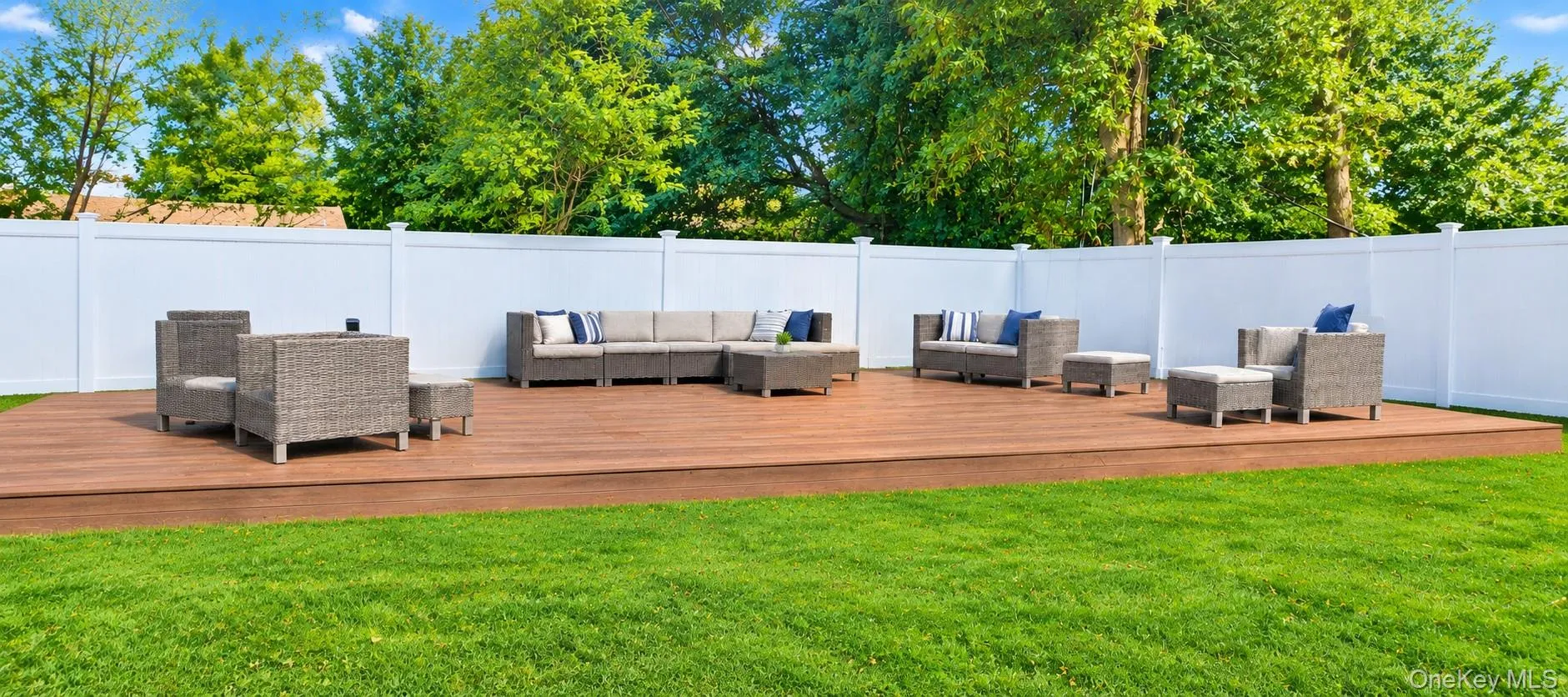 Expansive deck with a surrounding white privacy fence, featuring a lush green lawn and trees. Expansive deck with a surrounding white privacy fence, featuring a lush green lawn and trees.