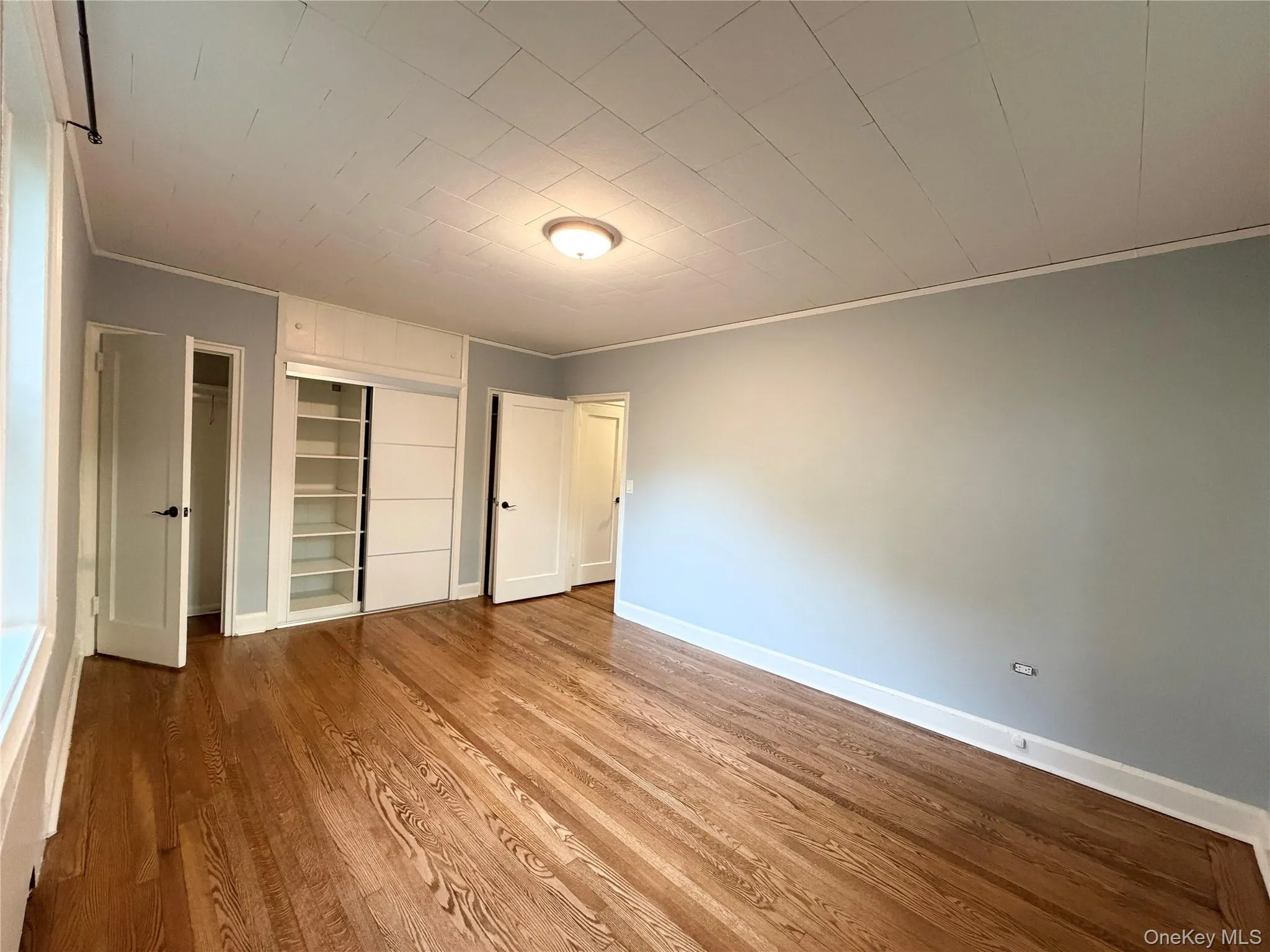 Hardwood flooring, built-in shelving, white trim, and a flush mount ceiling light Hardwood flooring, built-in shelving, white trim, and a flush mount ceiling light