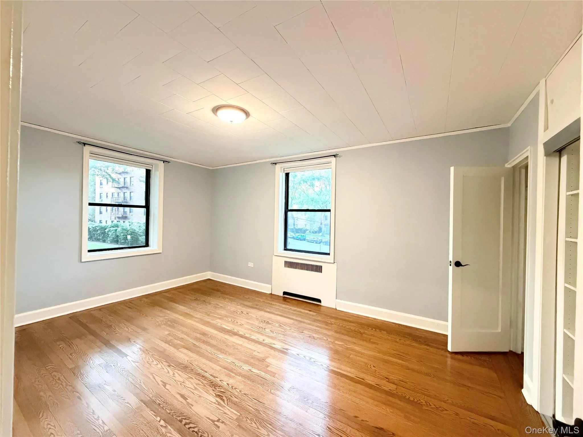 Hardwood flooring, light-toned wall paint, two windows, ceiling-mounted light fixture, and a white interior door with dark hardware Hardwood flooring, light-toned wall paint, two windows, ceiling-mounted light fixture, and a white interior door with dark hardware