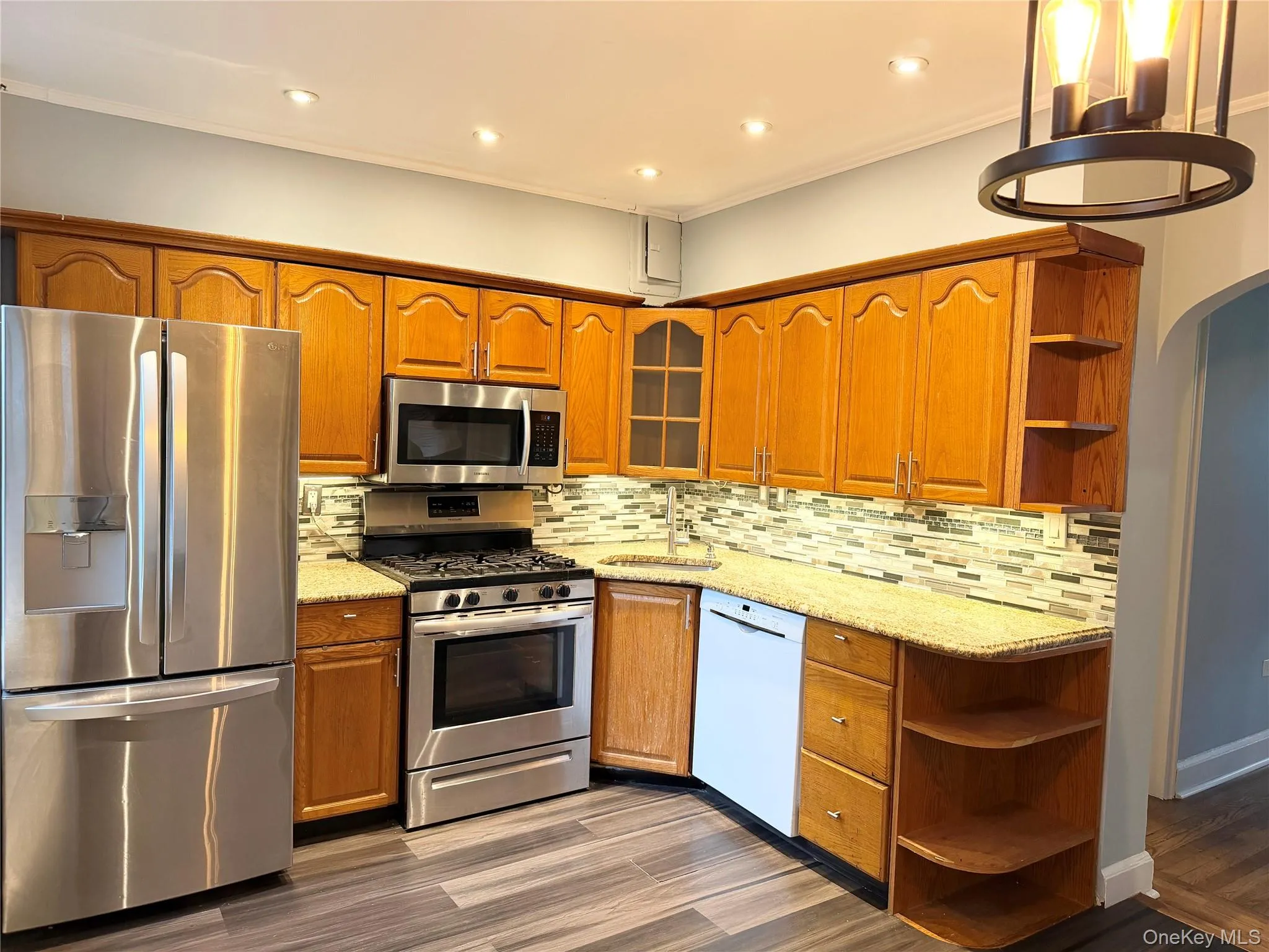 Kitchen featuring stainless steel appliances, wood-finish cabinetry, patterned tile backsplash, recessed lighting, and wood-finish flooring Kitchen featuring stainless steel appliances, wood-finish cabinetry, patterned tile backsplash, recessed lighting, and wood-finish flooring