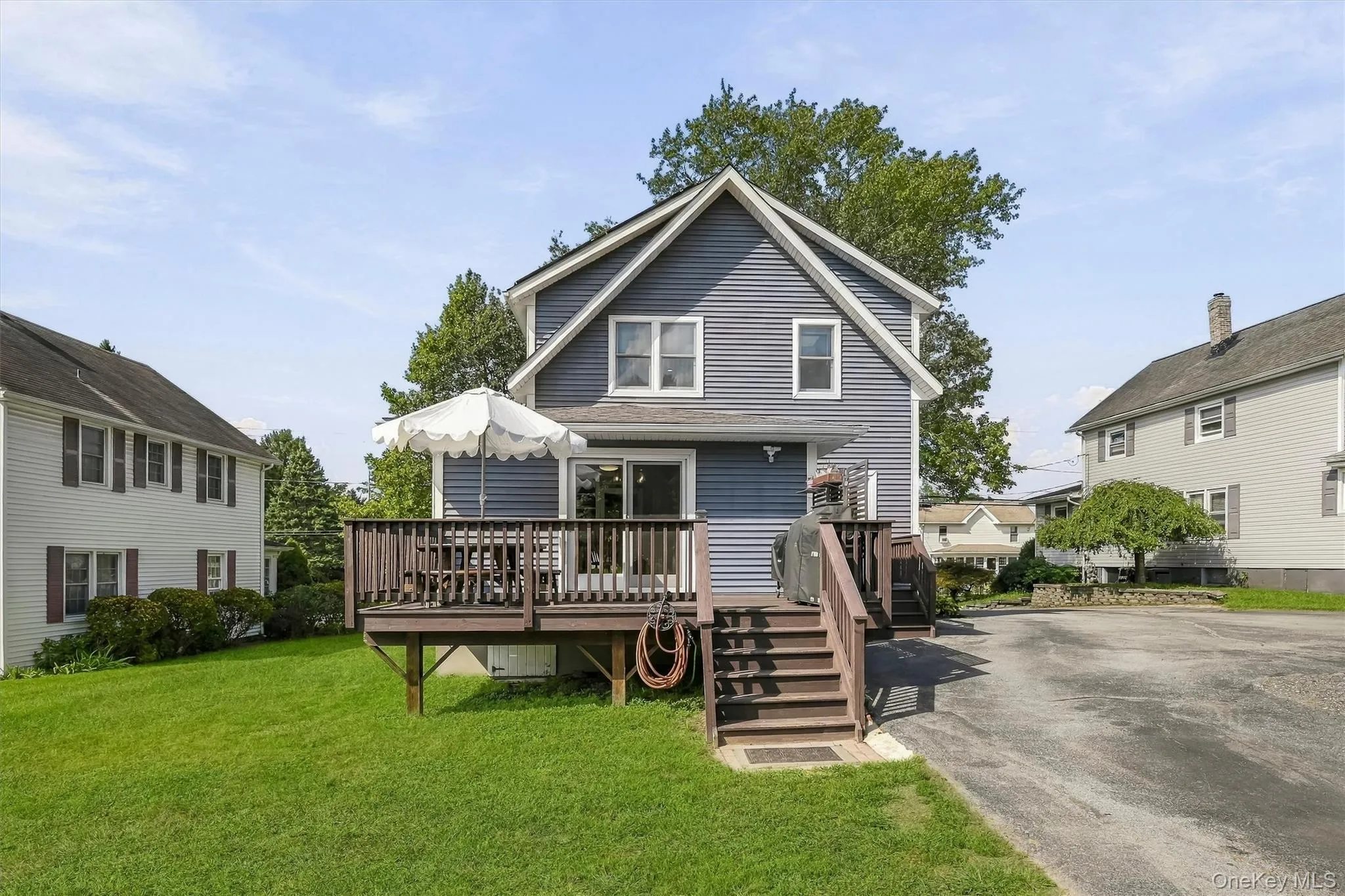 Rear exterior featuring a spacious wooden deck with railings and steps, sliding glass doors, and a manicured lawn Rear exterior featuring a spacious wooden deck with railings and steps, sliding glass doors, and a manicured lawn