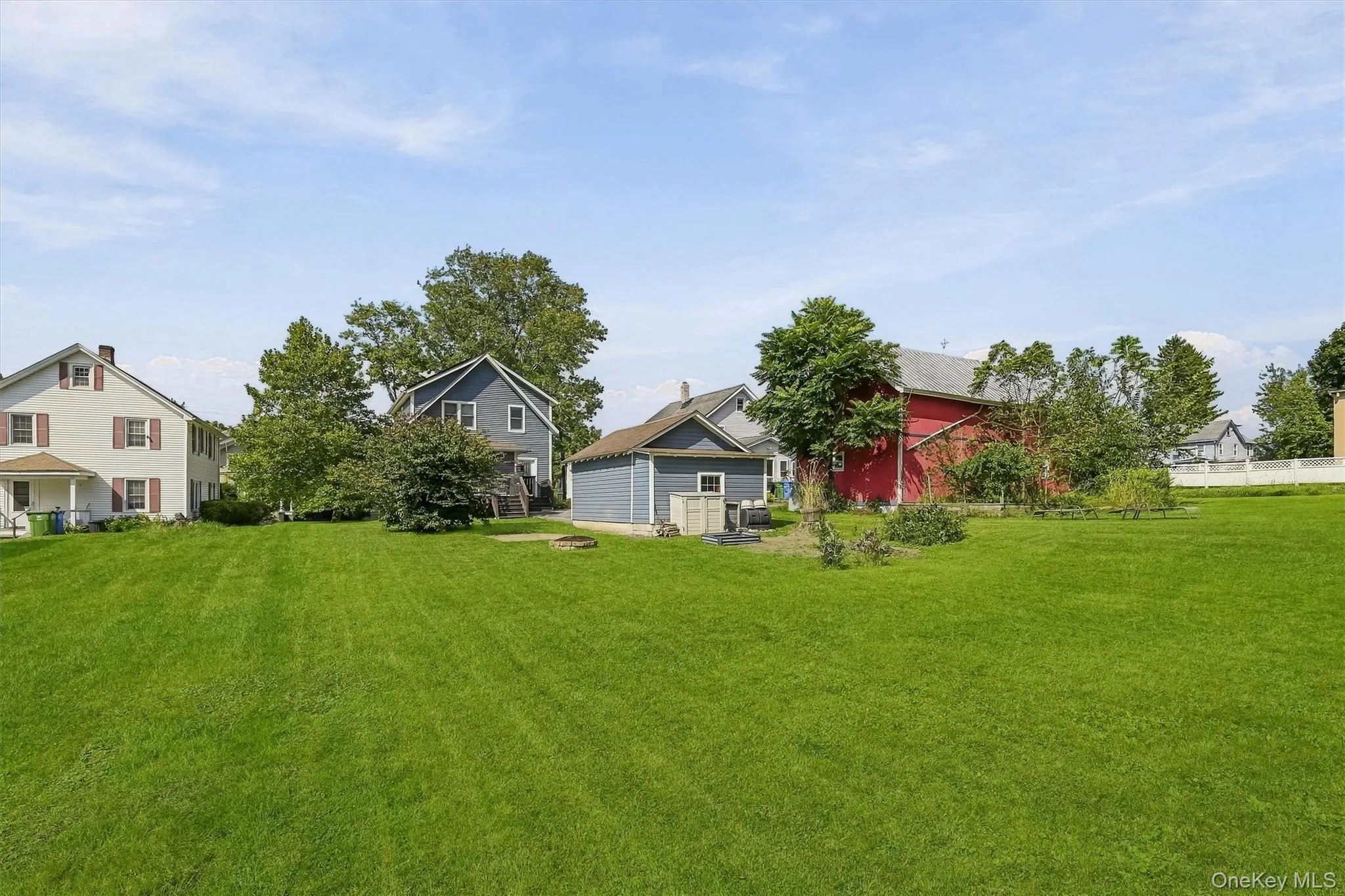 Expansive green lawn with mature trees, a detached storage shed, and a red barn structure Expansive green lawn with mature trees, a detached storage shed, and a red barn structure