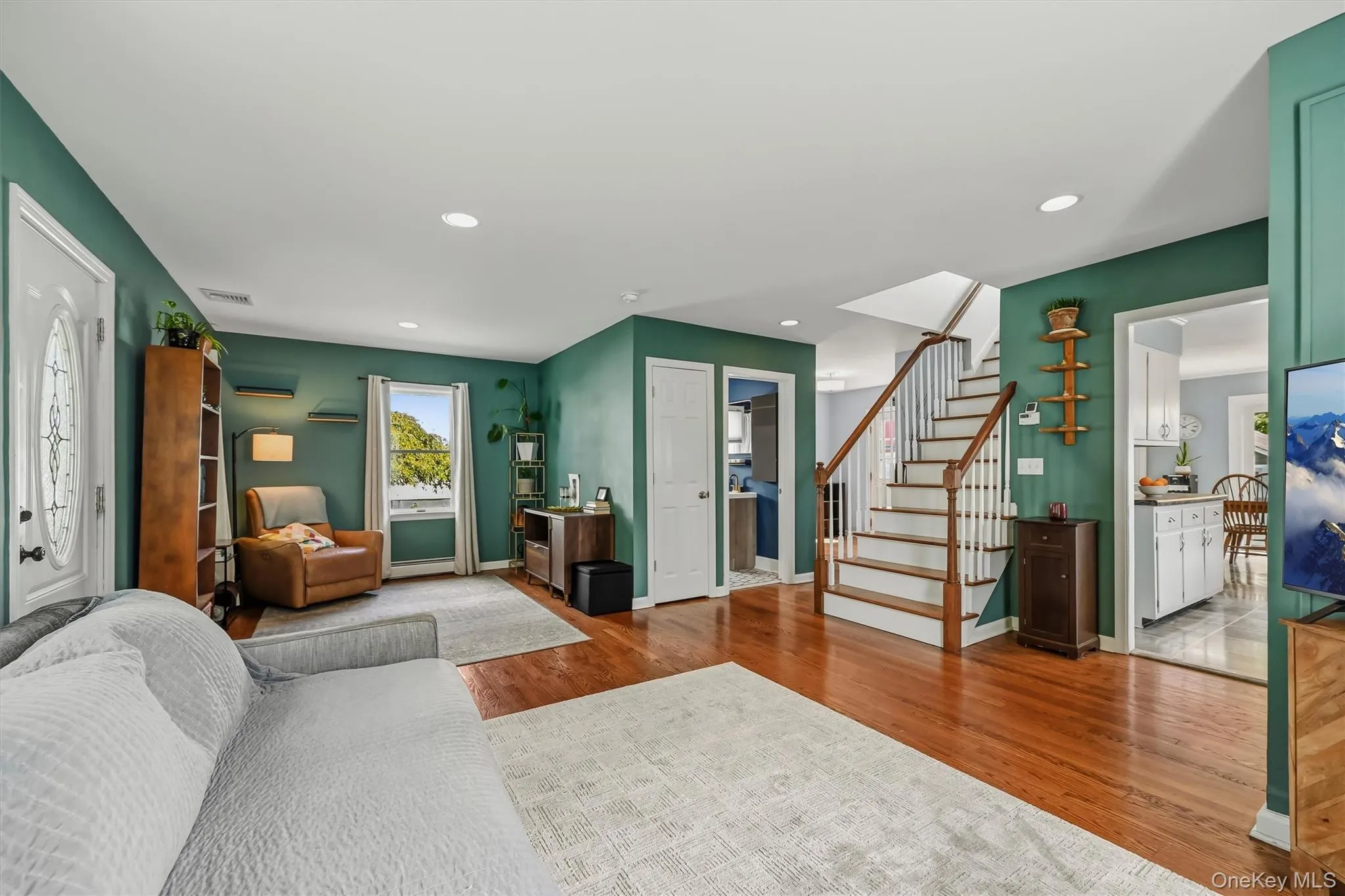 Hardwood flooring throughout, a white front entry door with decorative glass, recessed lighting, and a staircase featuring wood handrails with white balusters Hardwood flooring throughout, a white front entry door with decorative glass, recessed lighting, and a staircase featuring wood handrails with white balusters