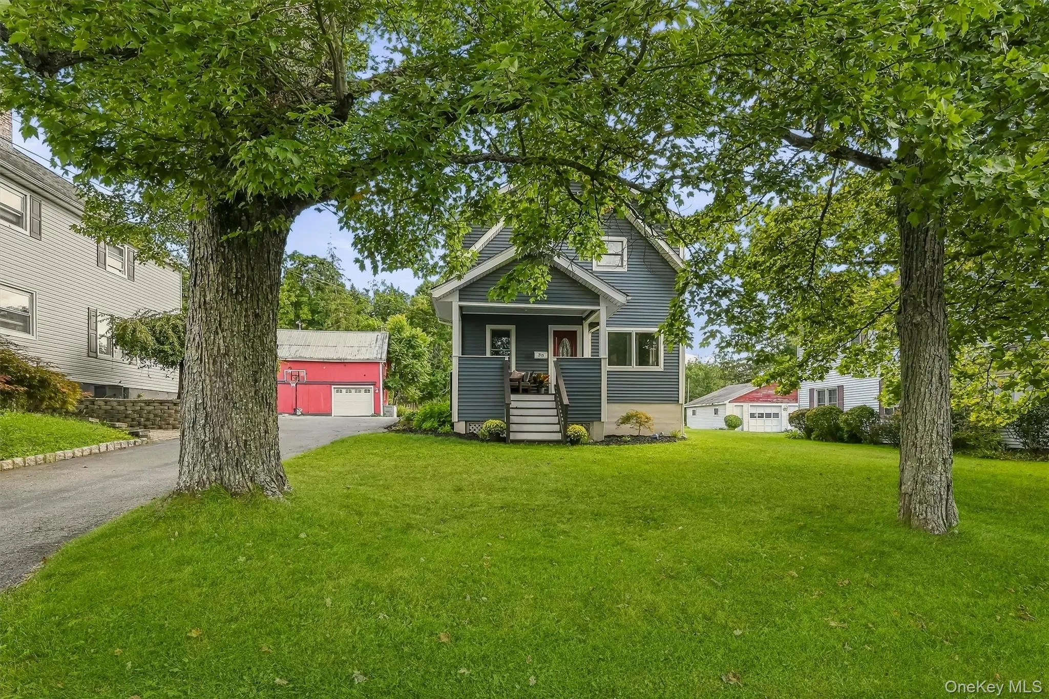 Two-story residence with a side-gabled roof, covered front porch, and mature trees on the front lawn Two-story residence with a side-gabled roof, covered front porch, and mature trees on the front lawn