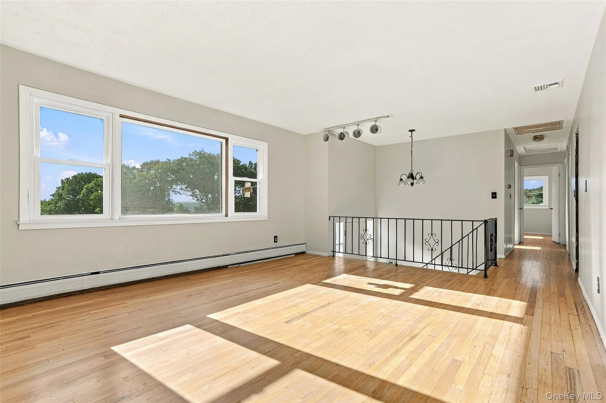 A view to the entrance with Hardwood flooring, expansive window, chandelier lighting, track lighting, and a wrought iron balustrade A view to the entrance with Hardwood flooring, expansive window, chandelier lighting, track lighting, and a wrought iron balustrade