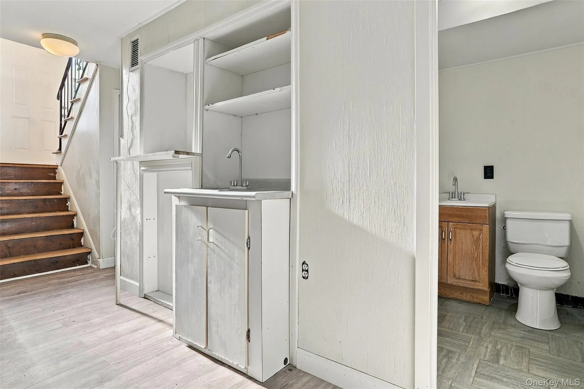 A view of the Poweder room in the lower level with Woodlike-finish flooring, built-in cabinetry with sink, wooden staircase with dark railing, and a separate room featuring a toilet and vanity A view of the Poweder room in the lower level with Woodlike-finish flooring, built-in cabinetry with sink, wooden staircase with dark railing, and a separate room featuring a toilet and vanity