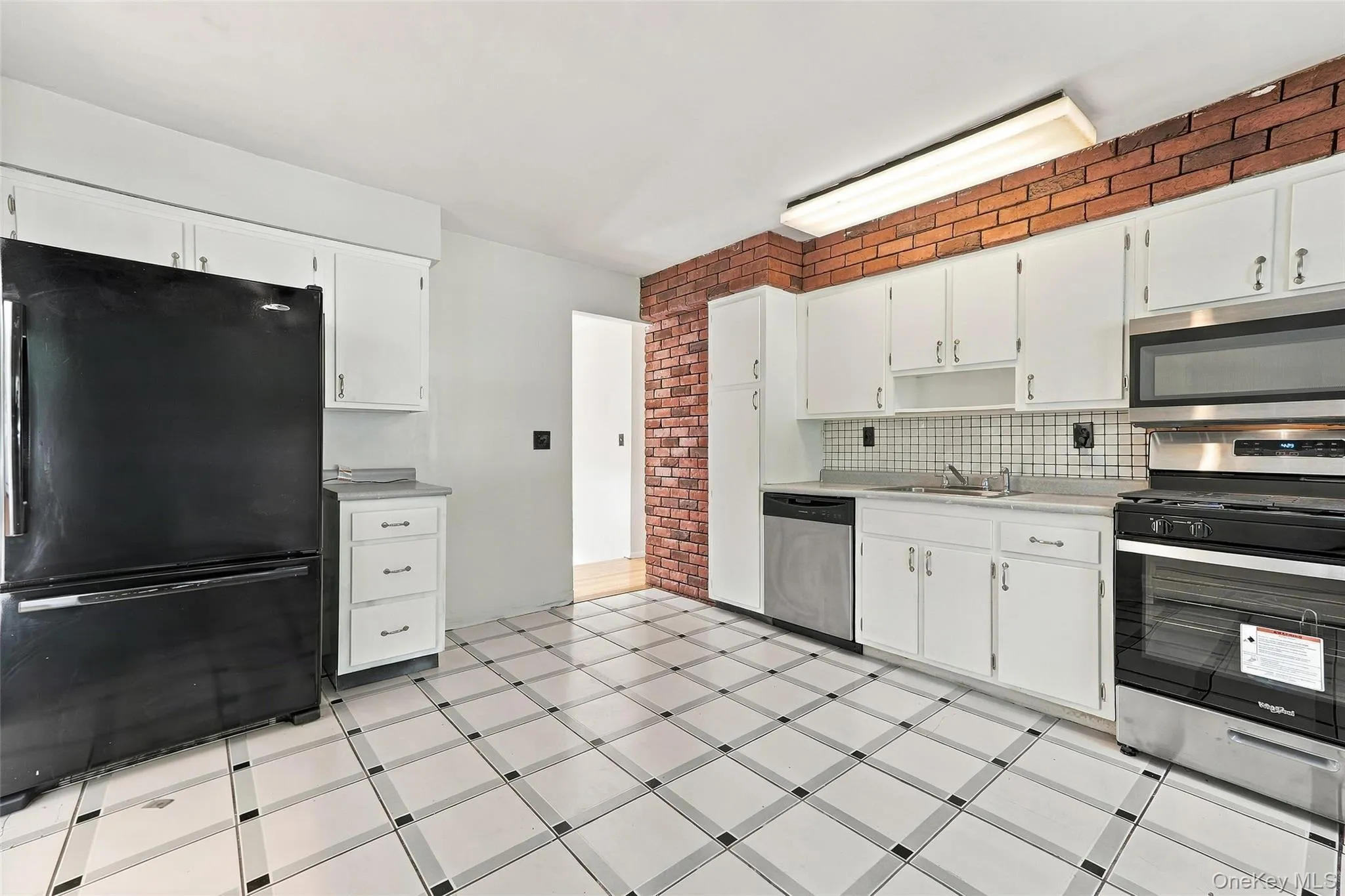 Kitchen featuring white cabinetry, a tile backsplash, stainless steel appliances, and a brick accent wall Kitchen featuring white cabinetry, a tile backsplash, stainless steel appliances, and a brick accent wall