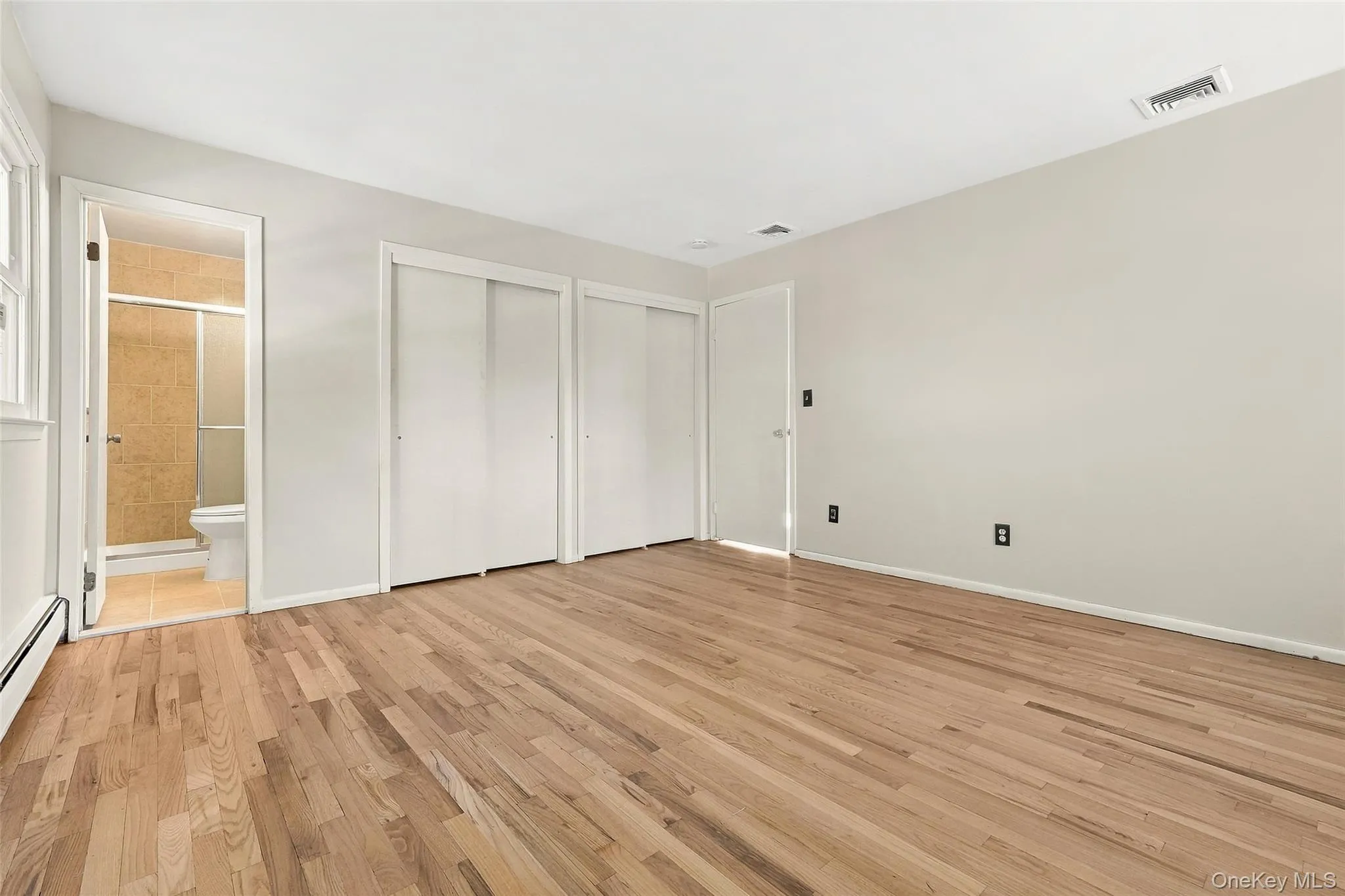 Primary Room with Hardwood flooring, multiple sliding closet doors, a window, and an attached bathroom with a shower enclosure Primary Room with Hardwood flooring, multiple sliding closet doors, a window, and an attached bathroom with a shower enclosure