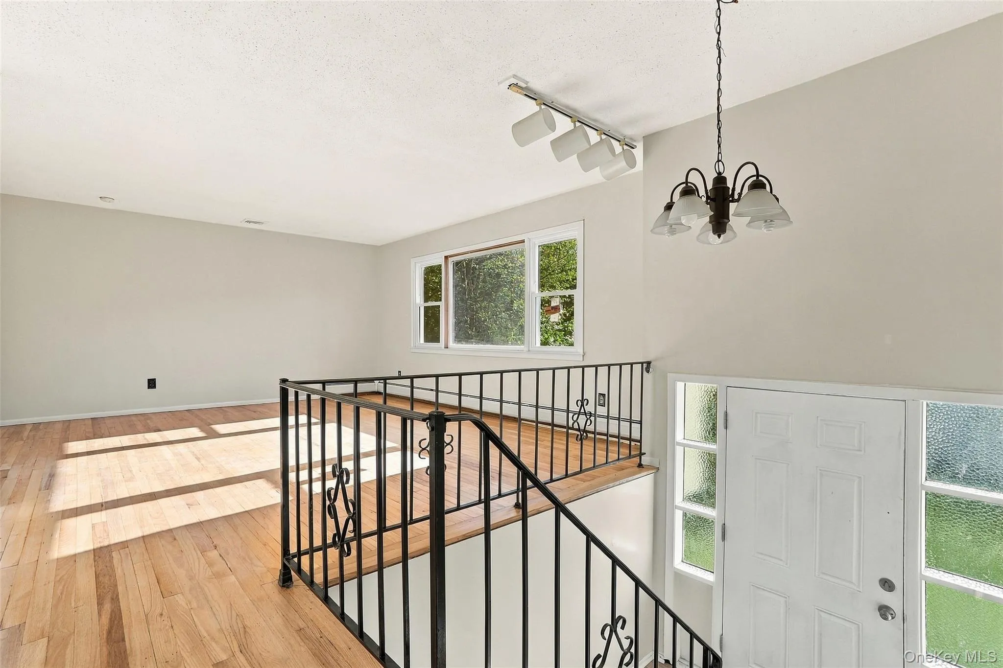Hardwood flooring, wrought iron railing, white paneled entry door, transom and sidelight windows, and a multi-light chandelier Hardwood flooring, wrought iron railing, white paneled entry door, transom and sidelight windows, and a multi-light chandelier