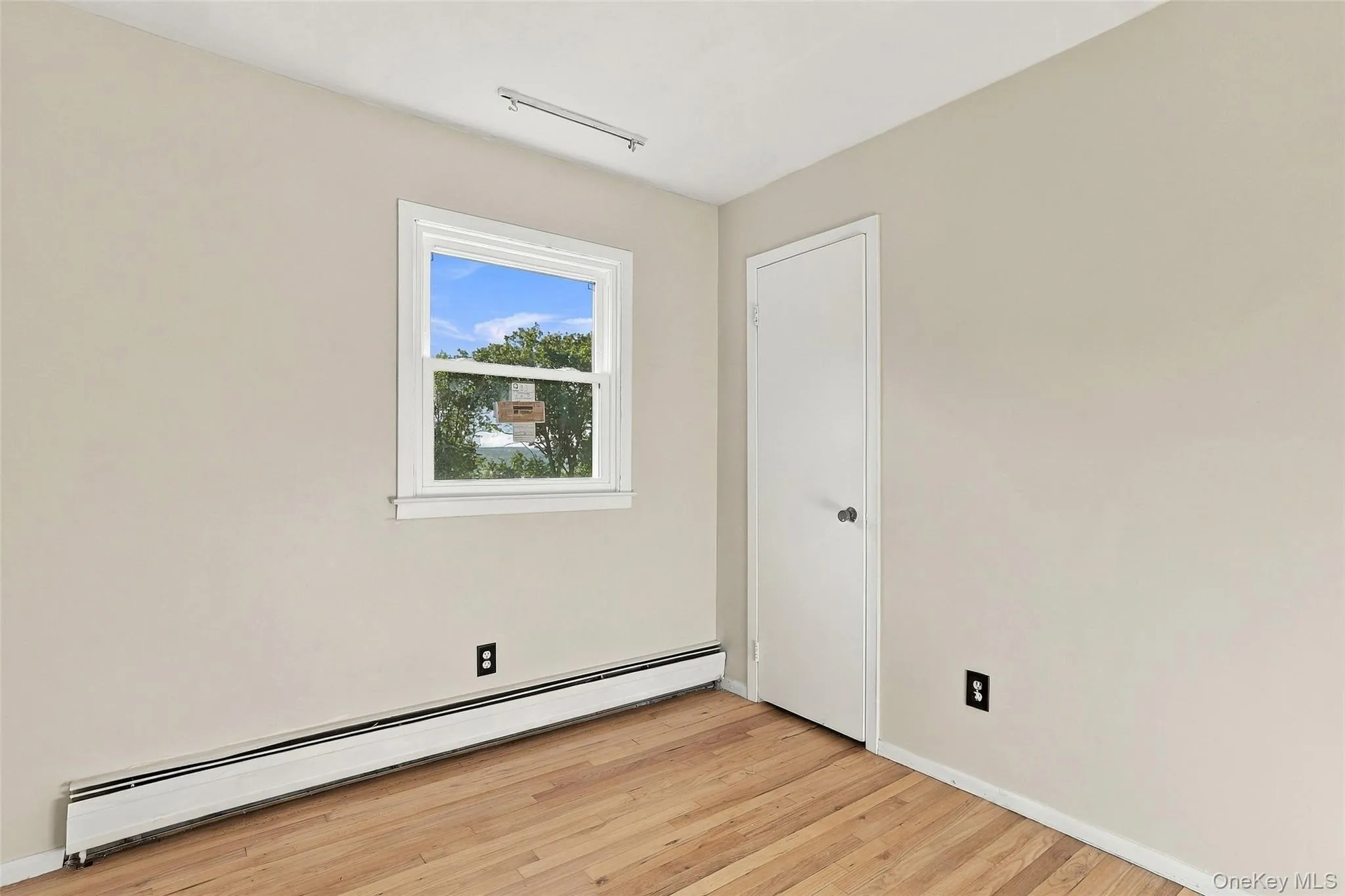 Bedroom with Wood-finish flooring, white trim, and a double-hung window Bedroom with Wood-finish flooring, white trim, and a double-hung window