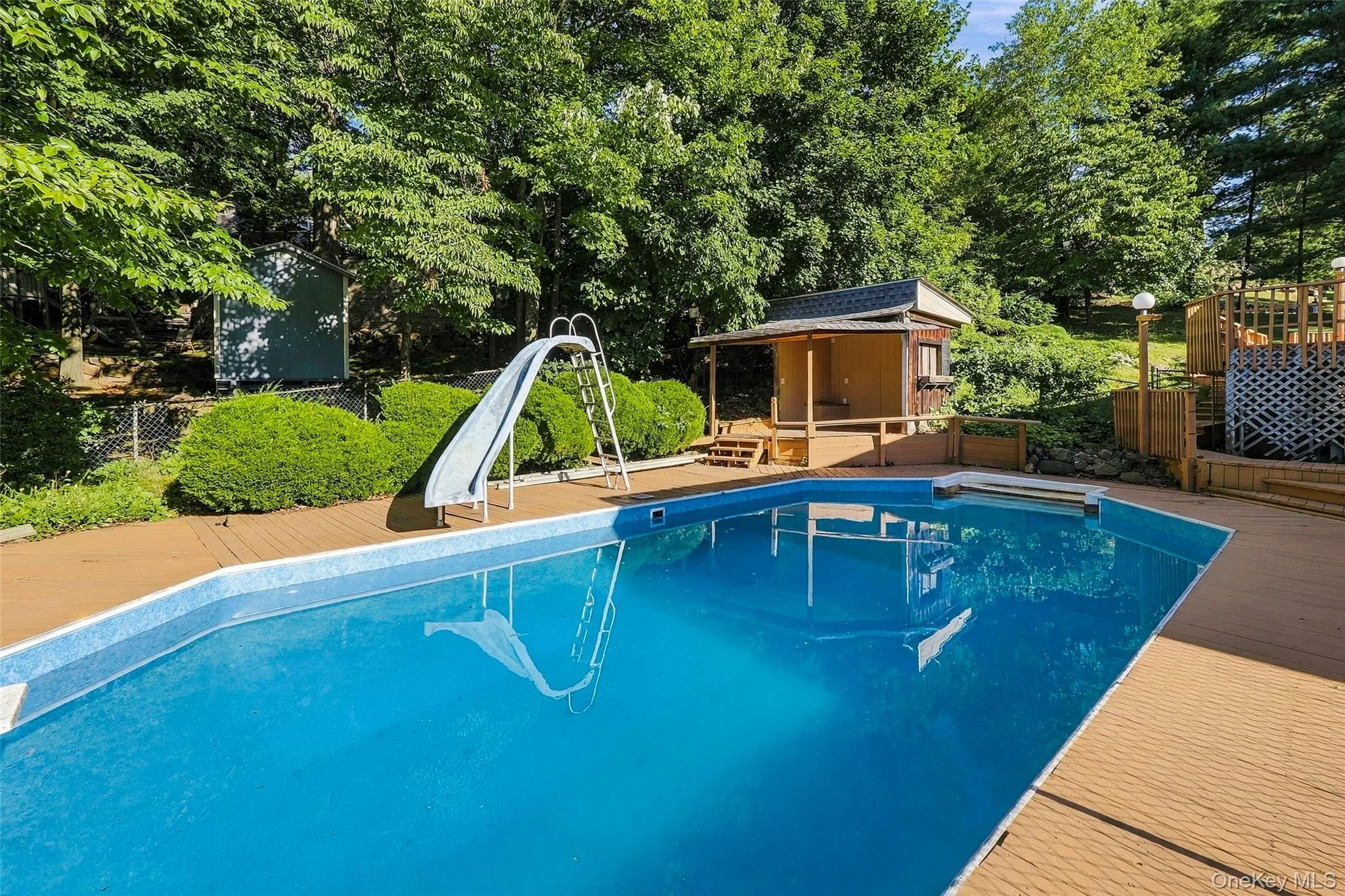 Expansive outdoor space featuring an in-ground swimming pool, surrounding wood-finish decking, and a separate pool house Expansive outdoor space featuring an in-ground swimming pool, surrounding wood-finish decking, and a separate pool house