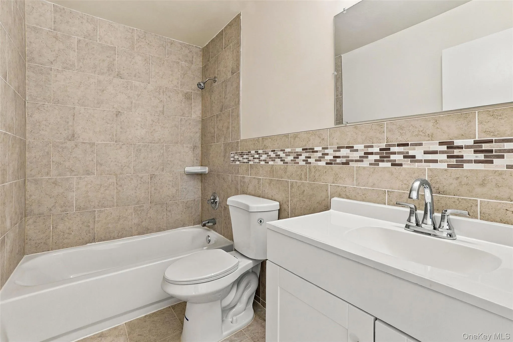 Built-in bathtub with a shower fixture, tile surround, toilet, vanity with integrated sink, and a large mirror Built-in bathtub with a shower fixture, tile surround, toilet, vanity with integrated sink, and a large mirror