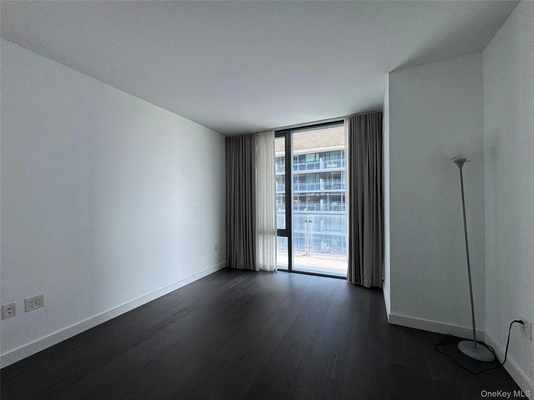 Dark wood-finish flooring with white baseboards, floor-to-ceiling windows, and white walls Dark wood-finish flooring with white baseboards, floor-to-ceiling windows, and white walls