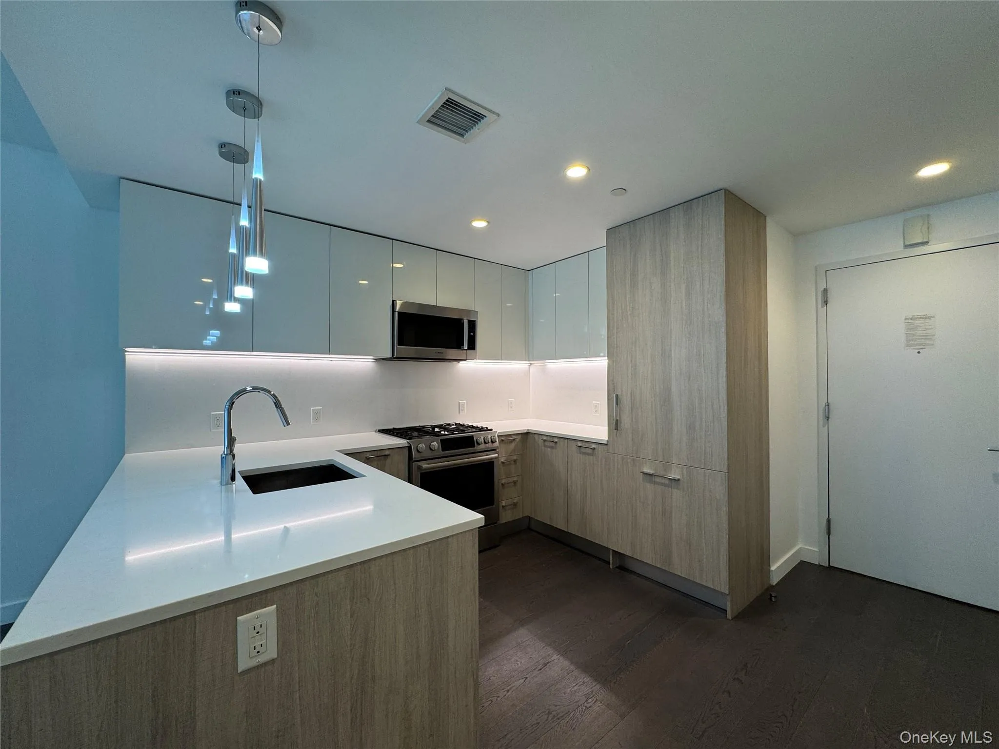 Contemporary kitchen featuring white solid surface countertops, stainless steel appliances, wood-finish cabinetry, and recessed lighting Contemporary kitchen featuring white solid surface countertops, stainless steel appliances, wood-finish cabinetry, and recessed lighting